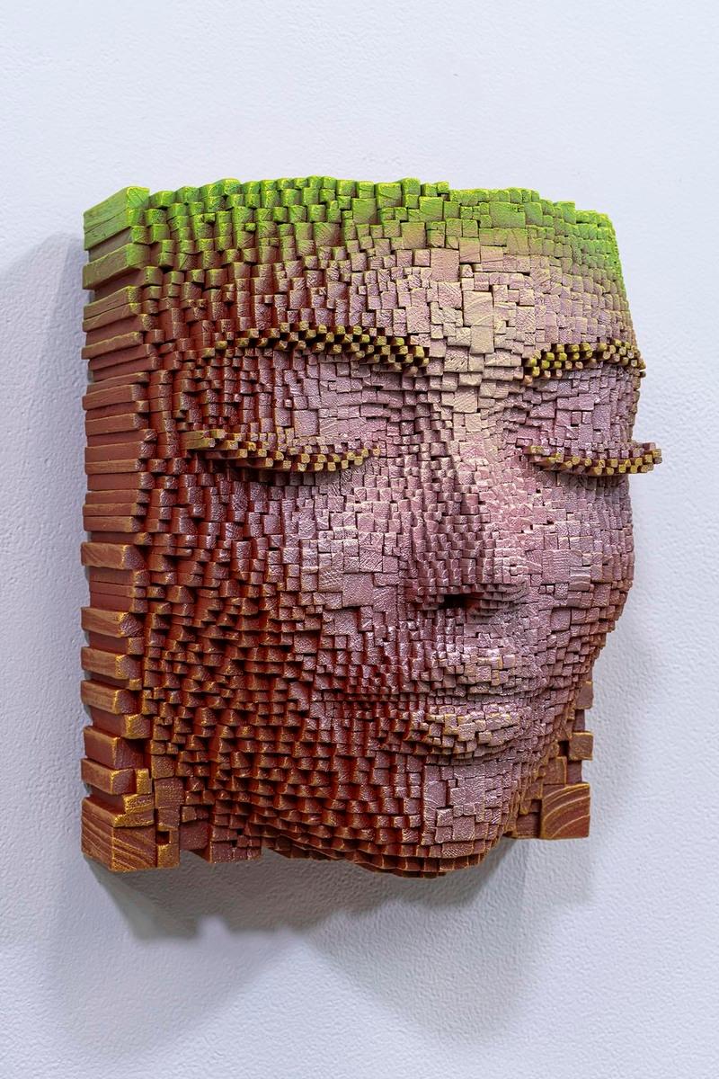 Questa affascinante opera d'arte presenta un volto scolpito in rilievo, composto da piccoli cubi di legno assemblati con eccezionale precisione. Le varie tonalità di marrone, rosa e verde creano un sottile gradiente, dando vita ed espressione al