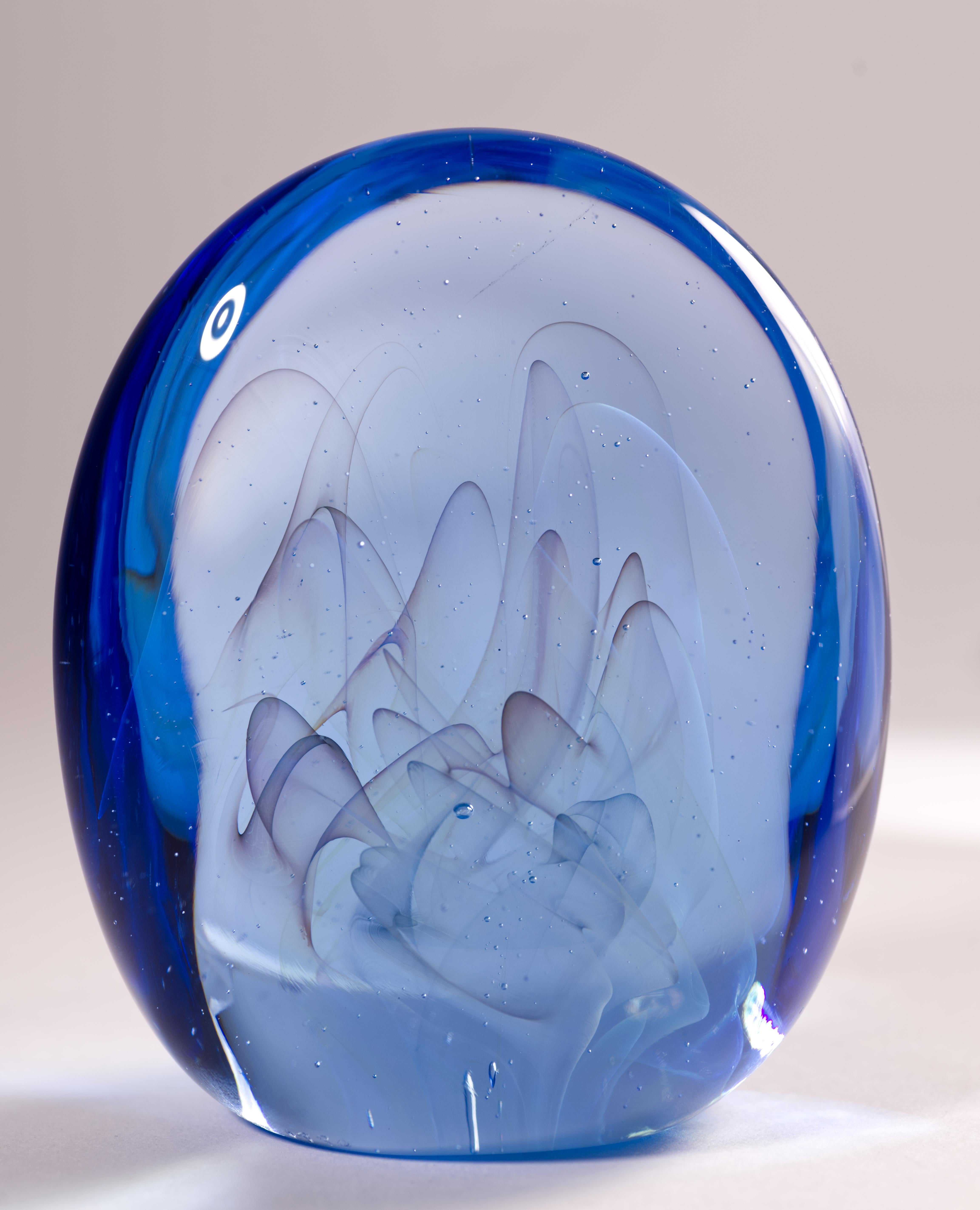  Cette sculpture en verre de studio ou presse-papier américain présente une forme organique allongée avec un motif interne voilé. Des bulles d'air contrôlées, dispersées à l'intérieur du verre, créent une illusion de mouvement et guident l'œil le