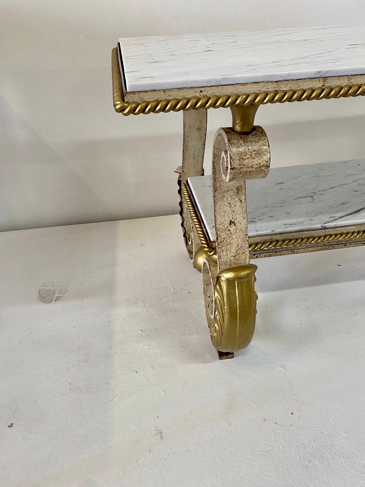 Scrolled iron legs with acanthus lead motif details. White marble newly replaced to both levels. Metal shows age and patina to demonstrate its actual vintage nature. Beautiful gold gilding painted to edges of marble - it is stunning! note: lower