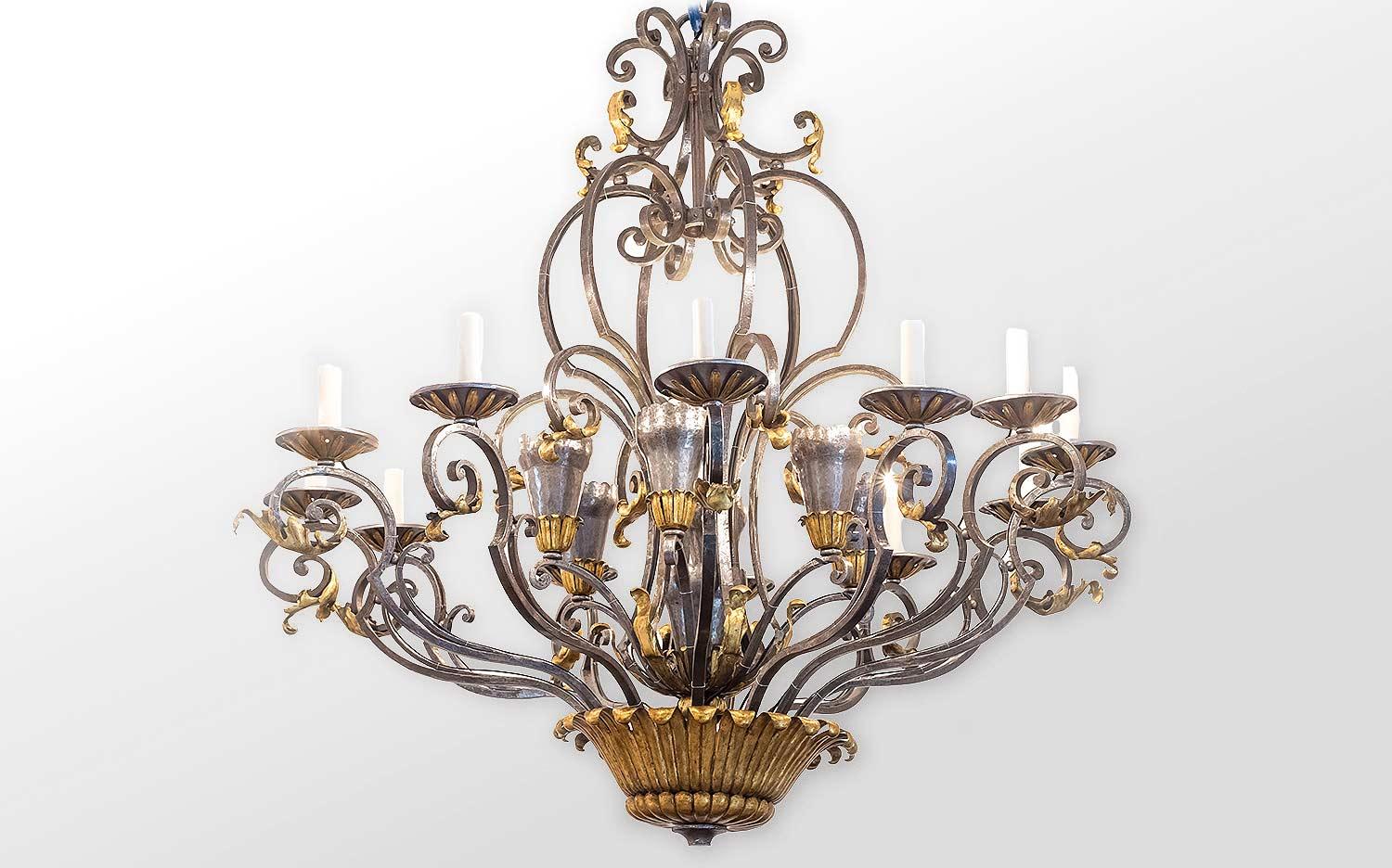 Gilbert Poillerat (in the style of). Wrought iron cage chandelier with 12 arm lights standing on a main cup adorned with waterleaves and gadroons. Candle crowns are also cup shaped, equally decorated with water leaves and the whole ensemble is