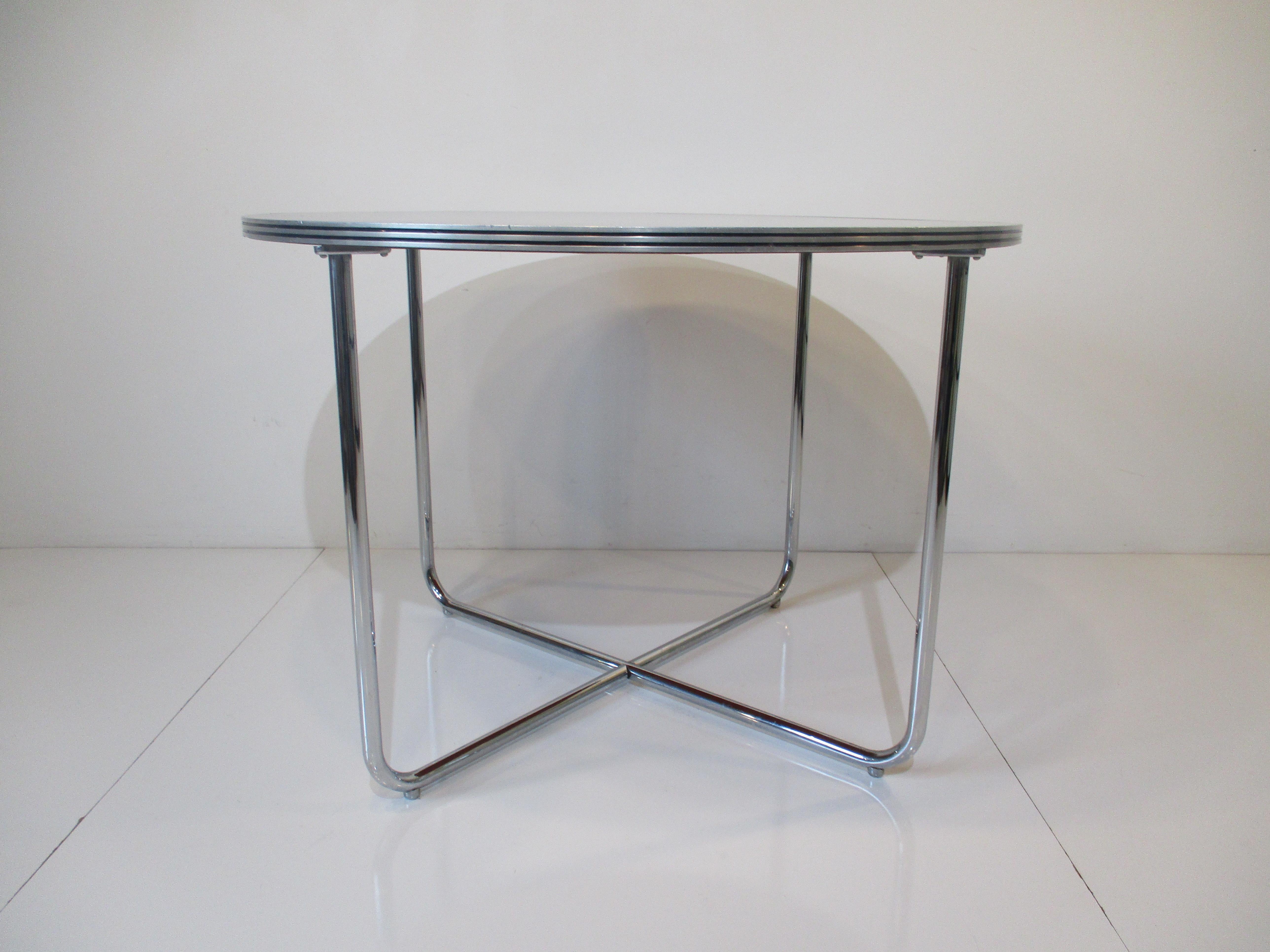 A chromed tubed X based dining table designed by the iconic Gilbert Rohde with triple banded aluminum edge and black permite Laminate top. A very well crafted piece from the Art Deco machine age period but can work with many interiors with it's