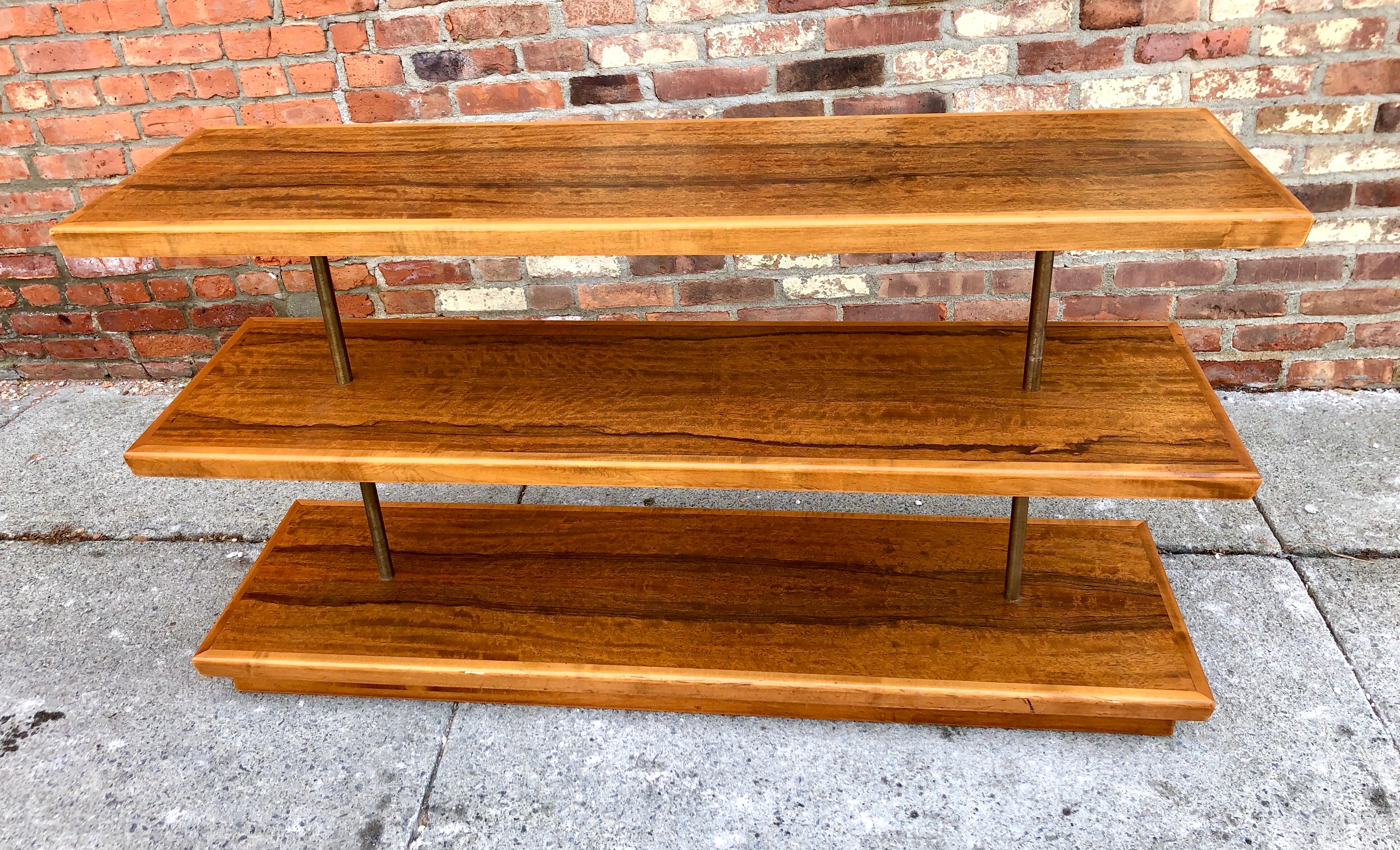 This rare three-tiered open étagère for the Herman Miller Furniture Company has beautifully figured East Indian Laurel veneer connected by two brass columns, raised on a plinth base, circa 1934, American. Model number 3454, the bookshelf measures