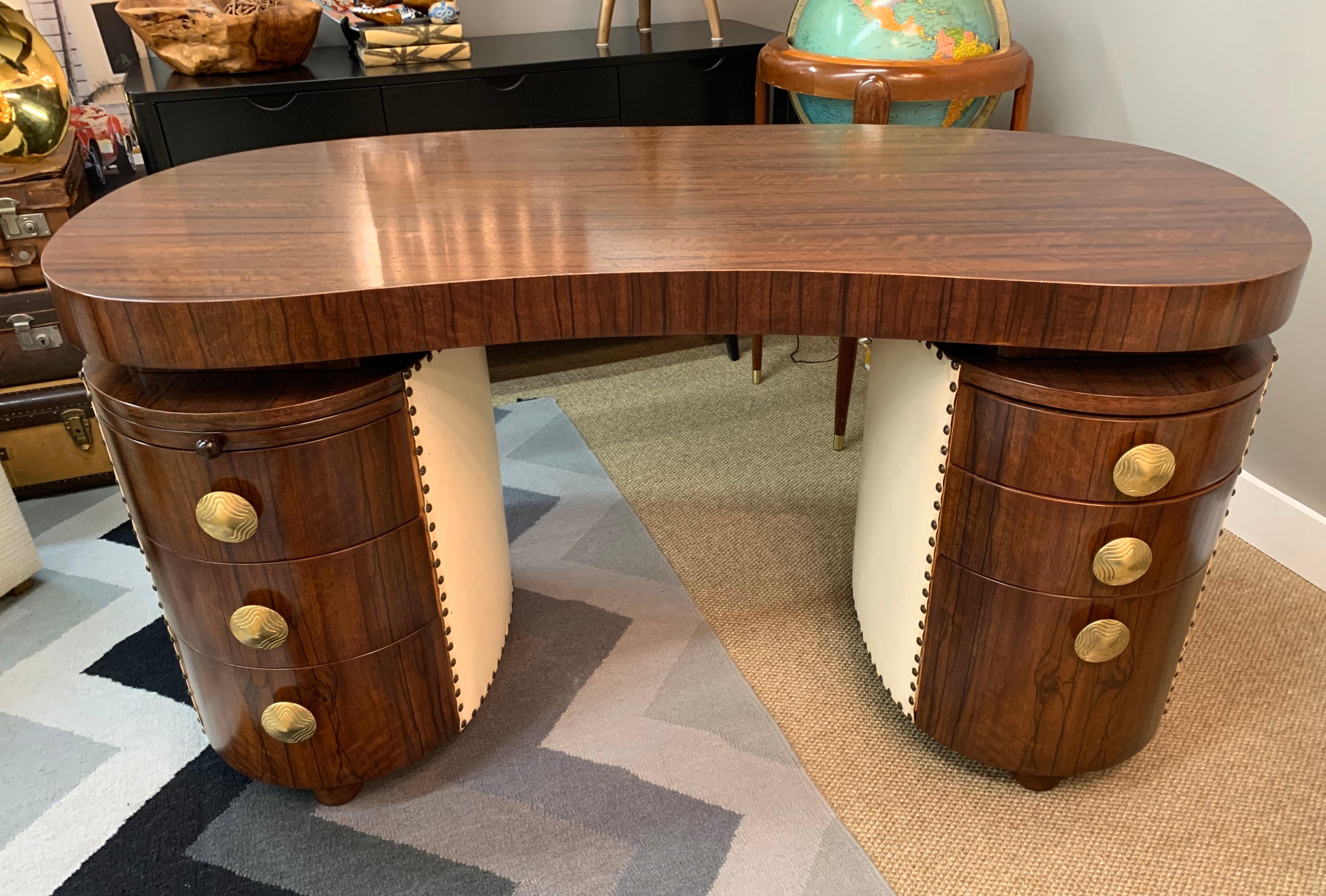Stunning and in excellent condition, an Art Deco kidney shaped desk designed by Gilbert Rohde, circa 1940 for Herman Miller. The heavy thick top is made of exotic paldoa wood and is supported by two oval cases of drawers wrapped in a cream leather