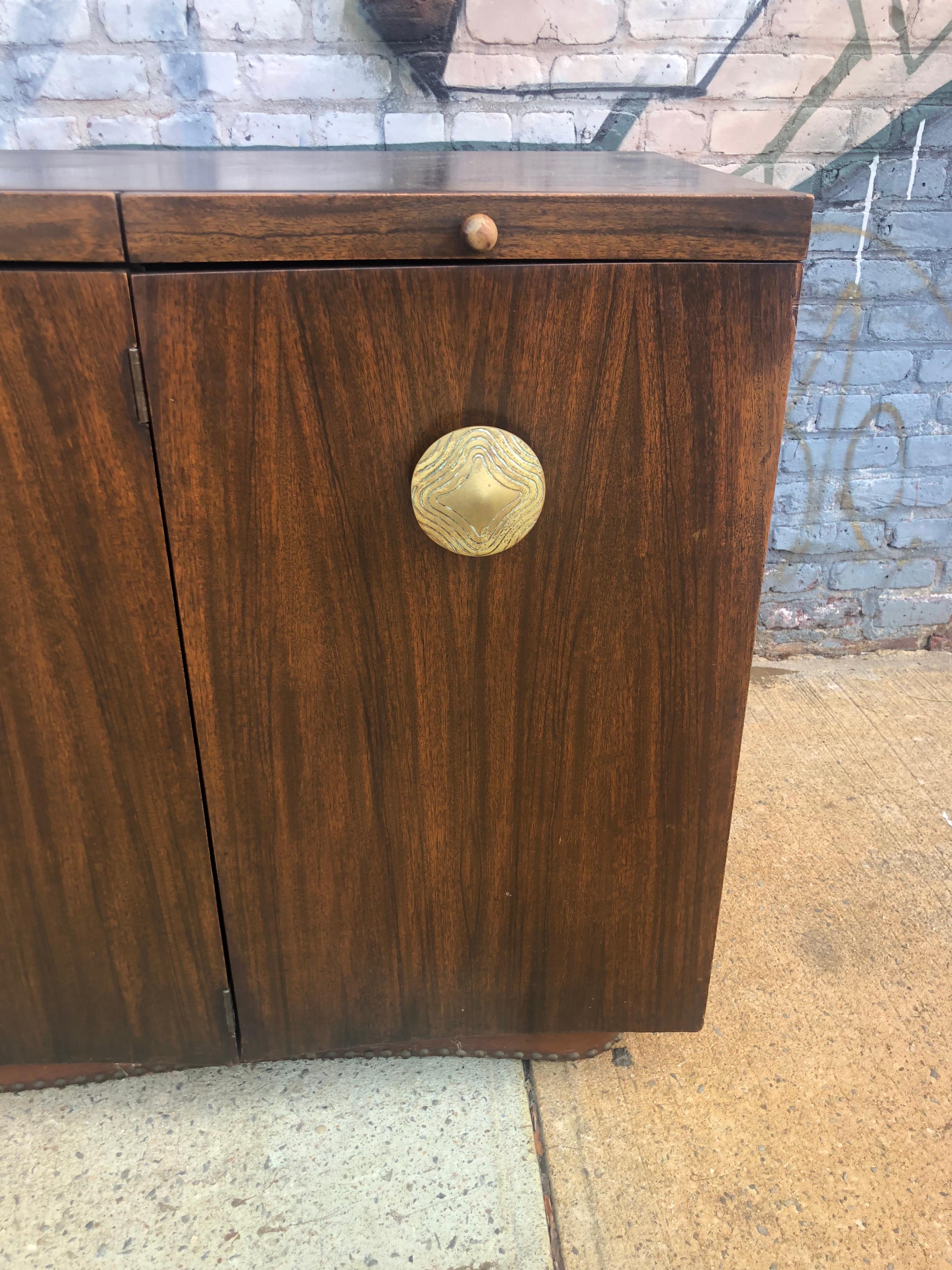 Handsome Gilbert Rohde Paldao series credenza for Herman Miller, circa 1940s Art Deco period piece featuring original cast brass pulls. Doors and drawers function. Cabinet rests on studded plinth base. A statement piece for the discerning collector.