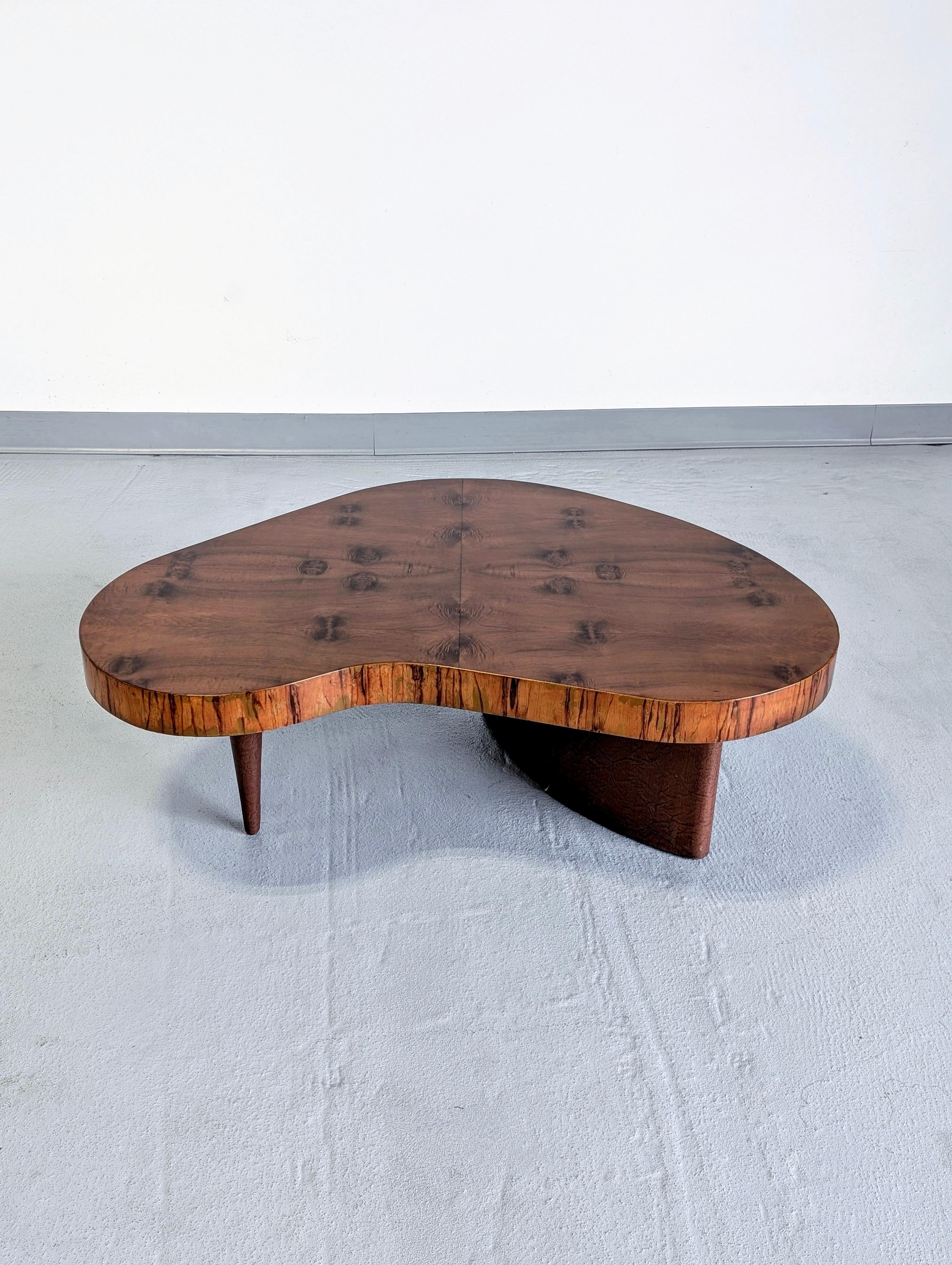Uncommon biomorphic design coffee table model #4186 designed by Gilbert Rohde for Herman Miller. Made from Paldao wood with original brown leatherette base. 
