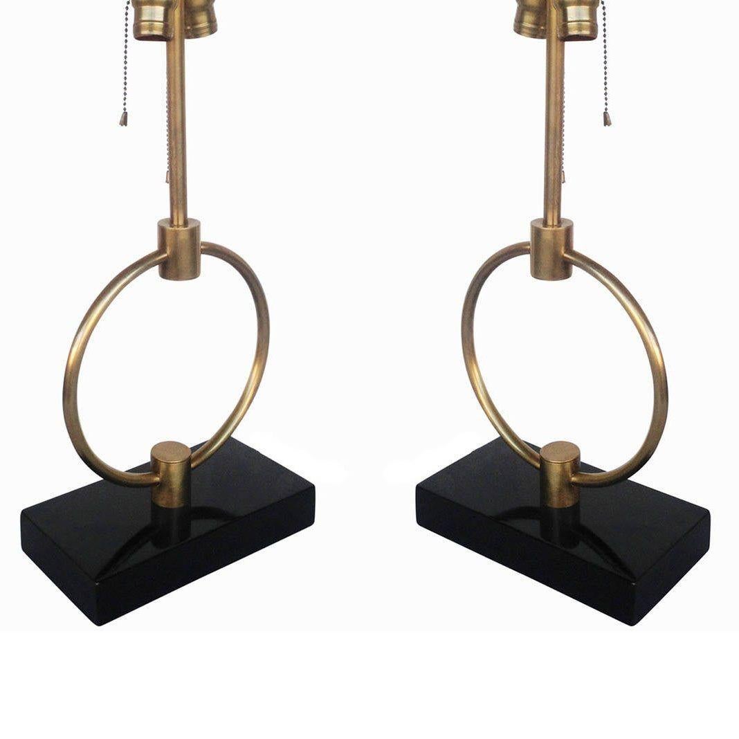 Fabriquée aux États-Unis, vers 1950, cette lampe de table à anneau en laiton de style Gilbert Rodhe présente un anneau central en laiton fixé à une base en bois laqué. Cette lampe a une forme élégante mais simple qui s'intègre facilement dans