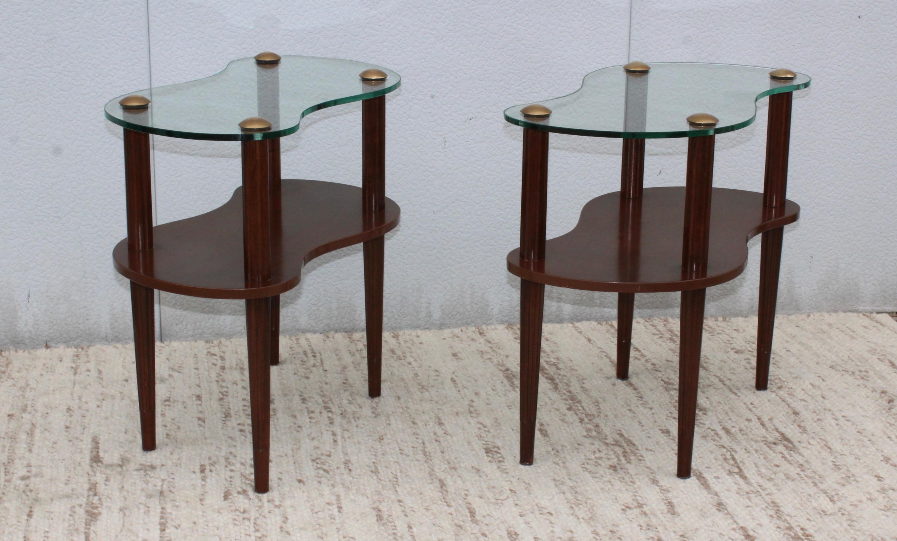 1950s two-tier wood and glass with solid brass caps end tables by Gilbert Rohde.