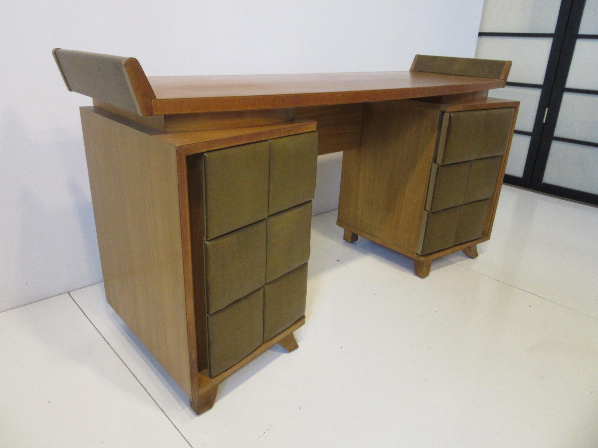 A early vanity or small desk with six angled leatherette padded drawers, floating top design and upturned angled sides with leatherette. Sitting on flared legs the piece is in a dark honey colored mahogany, well crafted by the Herman Miller