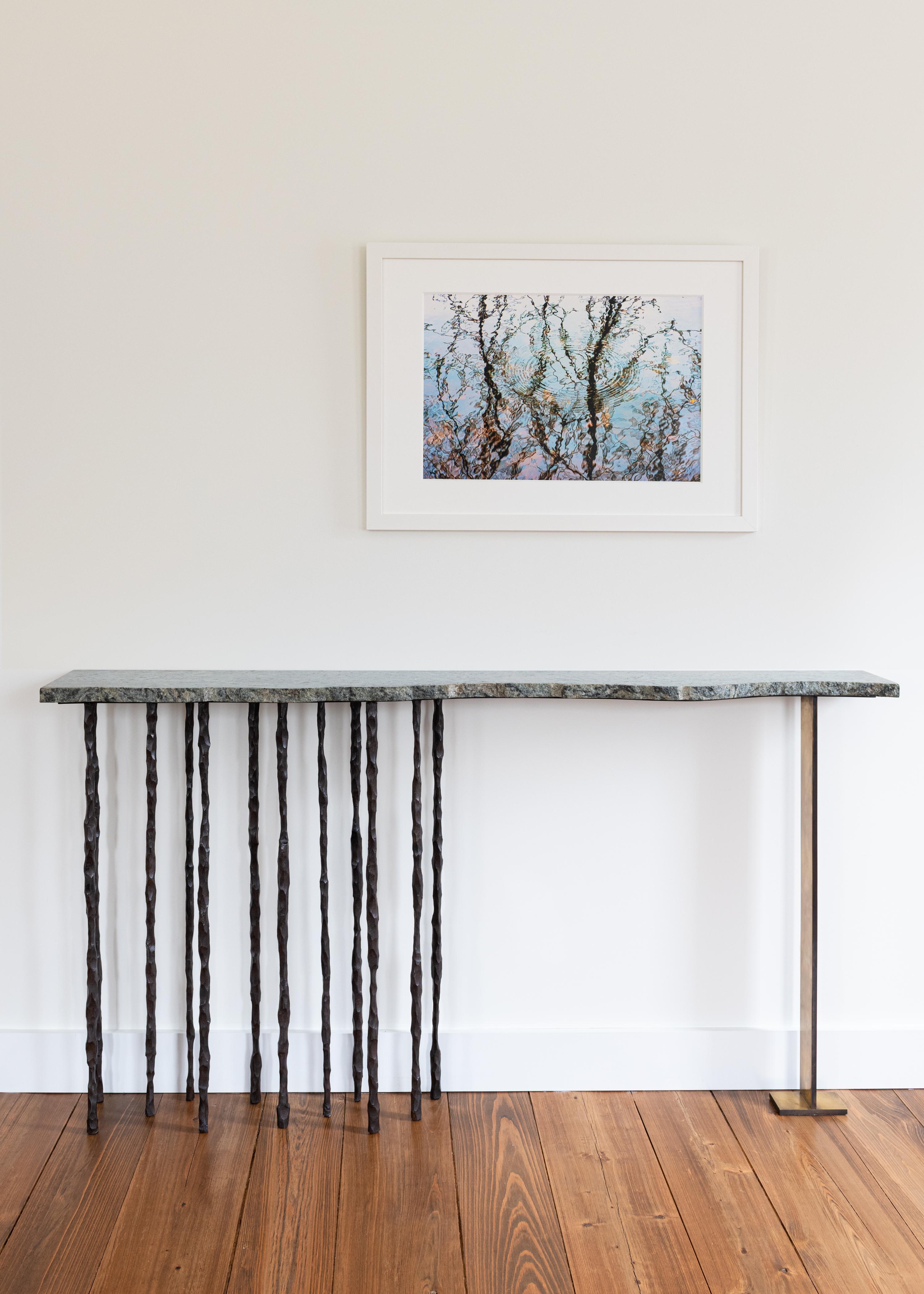 One of a kind handcrafted artisan sculptural console. Melding a unique stone slab with individually wrought and textured iron legs, this Stand alone piece of art has both strength and delicacy. By adding a rectangular brass leg with patina to the