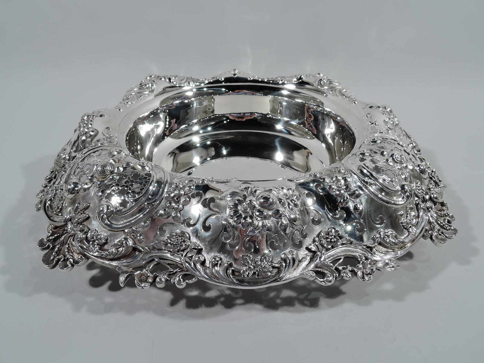 Gilded age sterling silver centerpiece bowl. Made by Tiffany & Co. in New York. Plain and round well. Turned-down and wavy rim embellished with scrolls, shells, flowers, and leaves. Ornament applied, pierced, and chased, and heightened with
