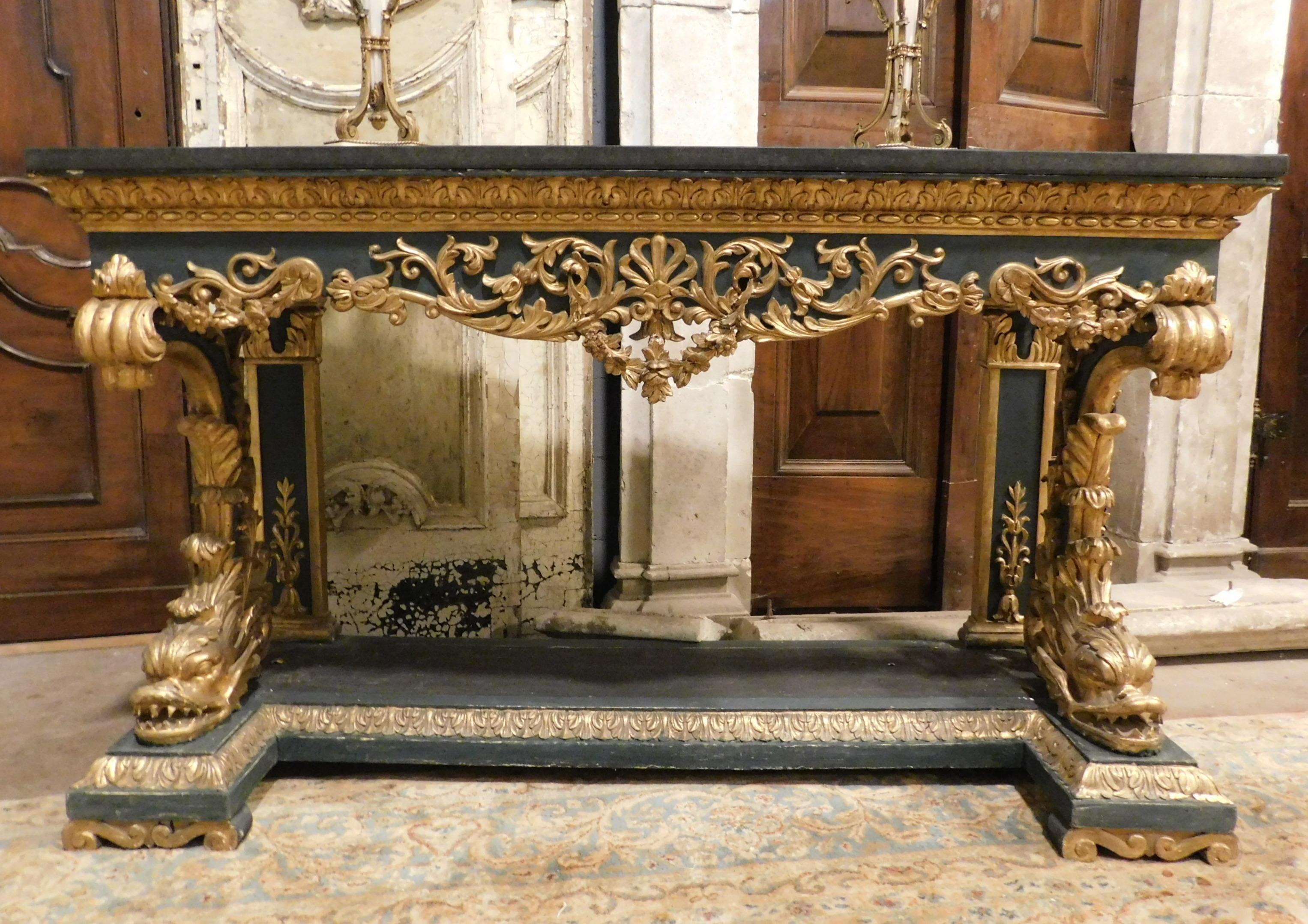 Richly hand-carved console with tritons and golden scrolls, lacquered on a black / dark green background, antique carved wooden base but with new black marble top (90s), hand-built in Italy.
Very tidy and super decorated, ideal for enriching a wall
