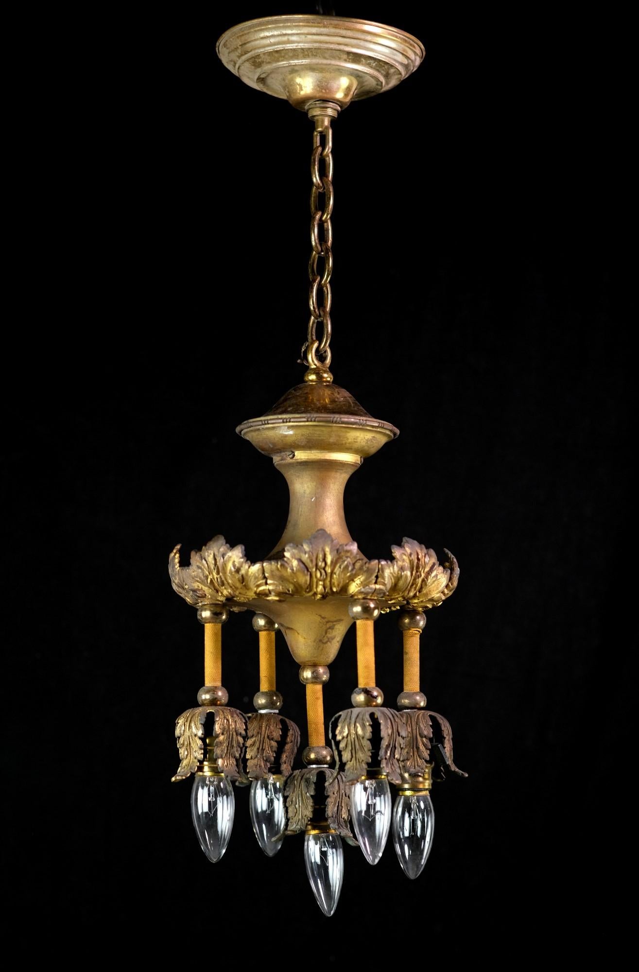 This antique cast bronze chandelier has elegant foliage details enhancing the top and bottom of each down light. There is a natural patina, and it is gold gilt which shows some wear. The arm of each light is wrapped in amber twine, which is original
