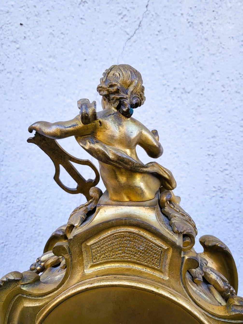 Kartell aus vergoldeter Bronze, gekrönt von einem Musikantenputto.  

Das Zifferblatt ist signiert L Milmann, Hersteller.   

Abnutzungserscheinungen an der Patina, Betrieb nicht garantiert.   

19. Jahrhundert.   

Höhe 46,5 cm.  
33.5 x 17cm.