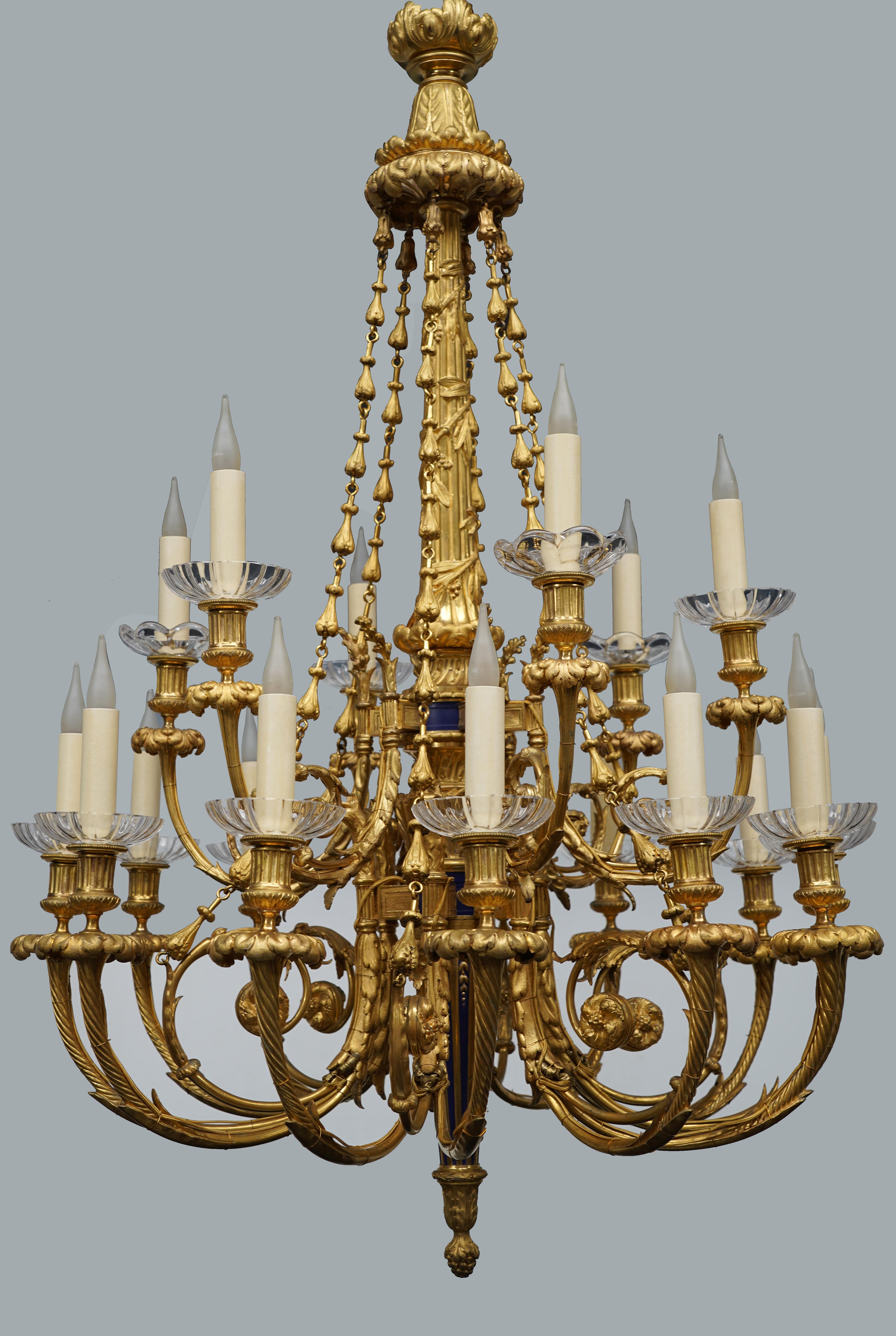 Important Louis XVI-inspired chandelier in gilded bronze with 18 lights. The baluster-shaped central shaft in blue enameled bronze is surmounted by a fluted rod in gilded bronze surrounded by intertwined laurel branches, topped with a leafy crown.