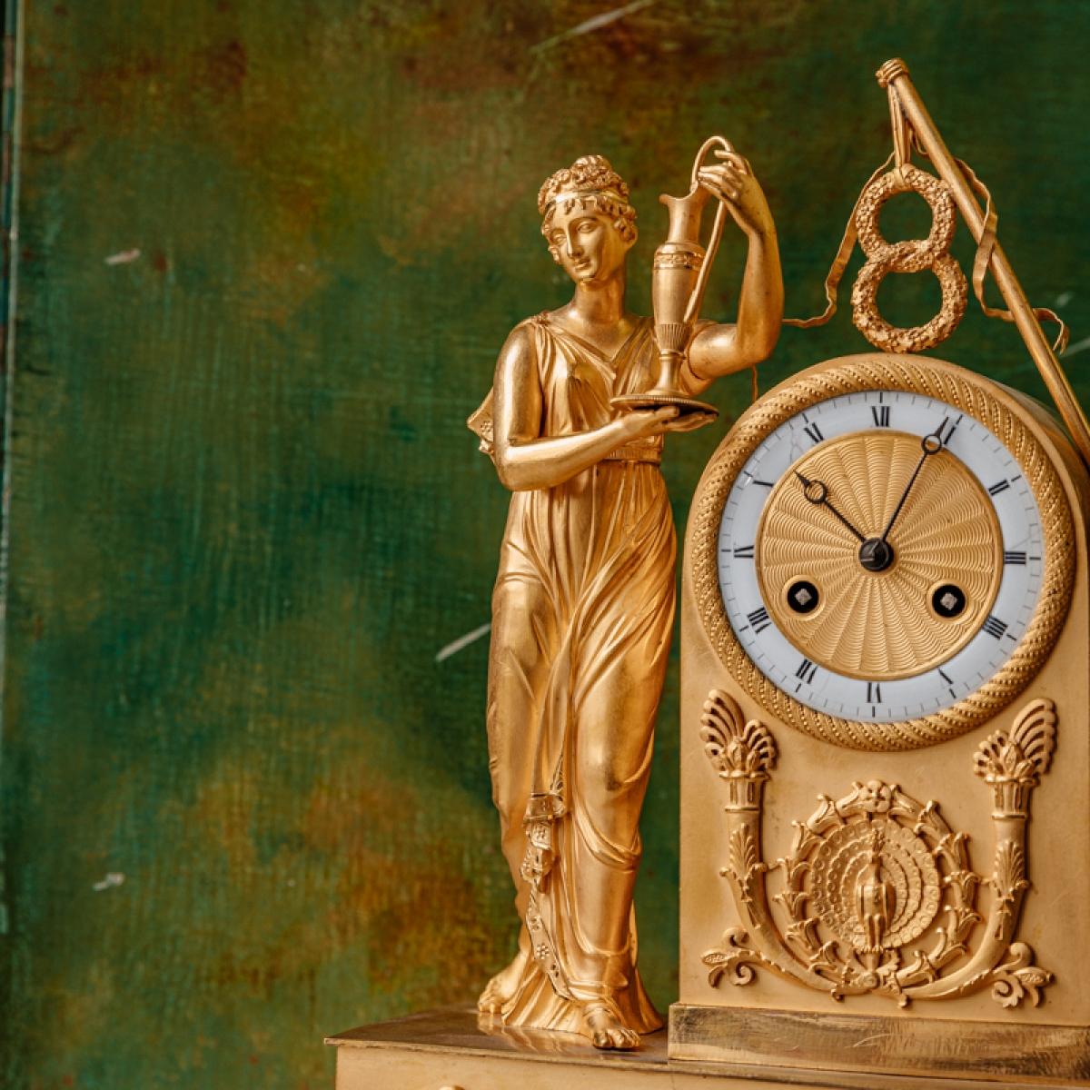 Gilded bronze clock
The gilding is original. 
The dial is white enamelled and the hours are written in Roman numerals.
Period: Restoration
Dimensions: H: 48,5, D: 12,5, W: 34,5 cm
Bollard type model, it represents the myth of the Goddess Hera.