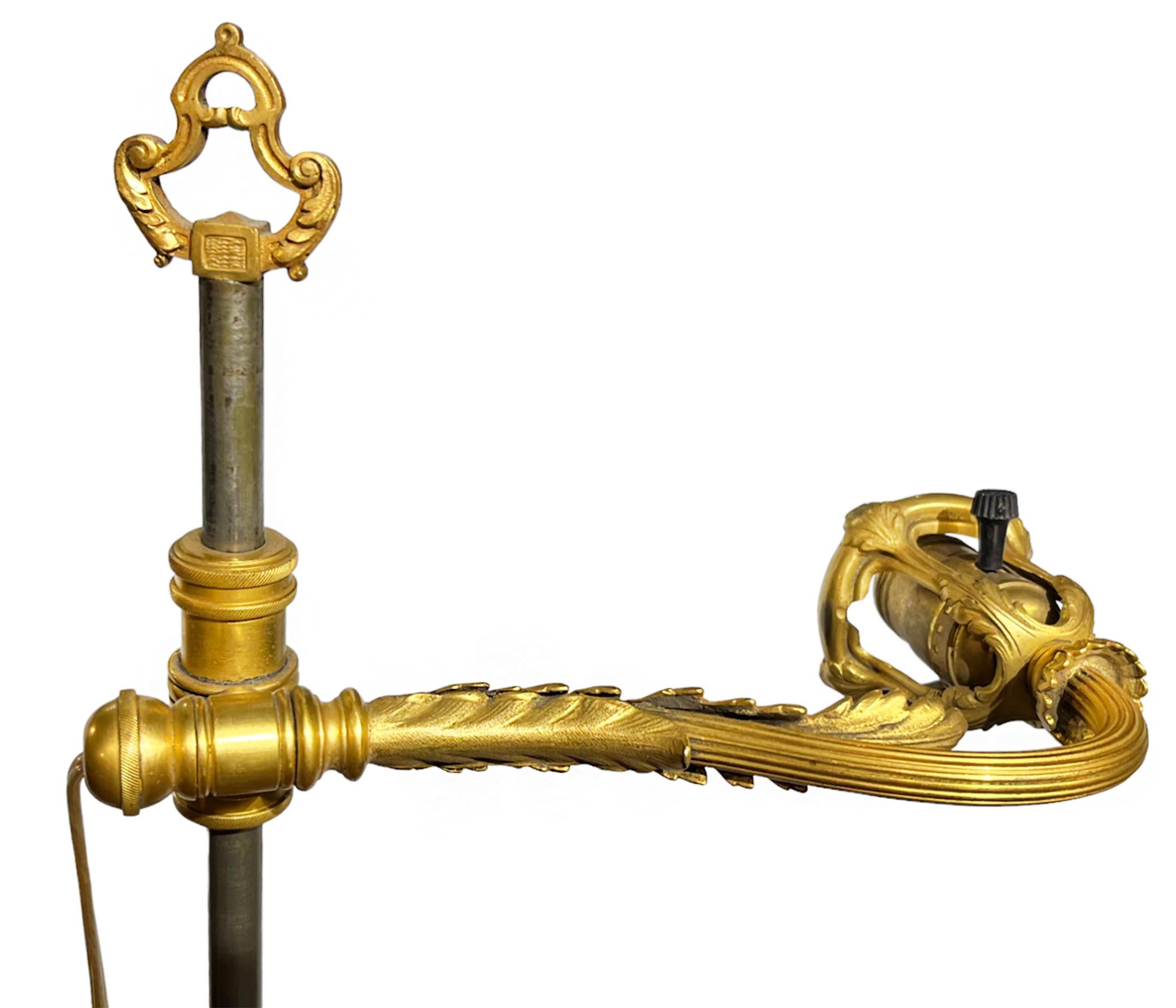 Diese fabelhafte antike Stehlampe von Edward F. Caldwell hat ein elegantes Design mit einem kräftigen Sockel aus vergoldeter Bronze mit Laubmotiv und Kranzlippe. Vom Sockel geht eine geriffelte Stange aus, die auf ein verziertes Gelenk trifft, das