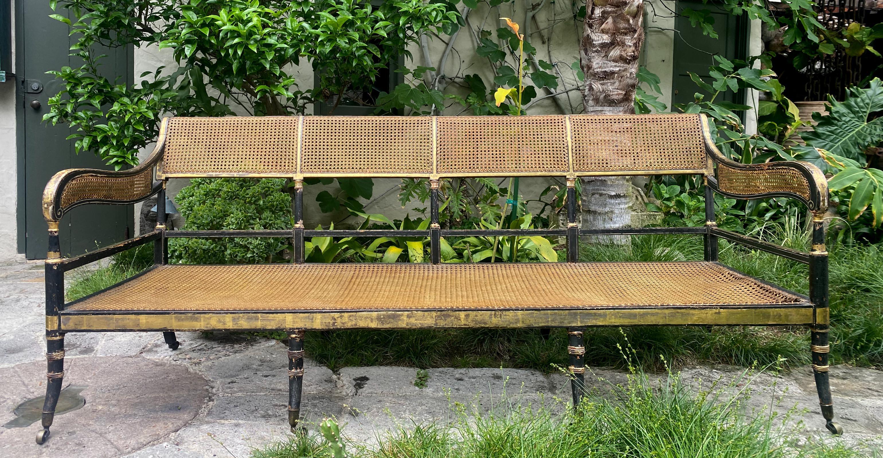 Stupendo divano a doghe dorato, tutto originale, realizzato con maestria e rifinito con una lucente lacca nera e raffinati accenti dorati. Riflettendo l'influenza classica del design dell'inizio del XIX secolo, questo pezzo presenta uno schienale