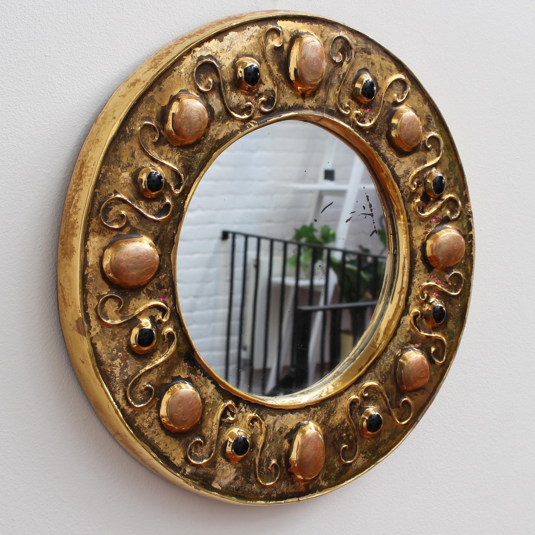 Gilded ceramic decorative wall mirror by François Lembo (circa 1960s-1970s). Porthole-shaped ceramic frame embellished with colourful enamelled cabochons in muted coral and black imitating natural stones. The piece is in fair vintage condition with