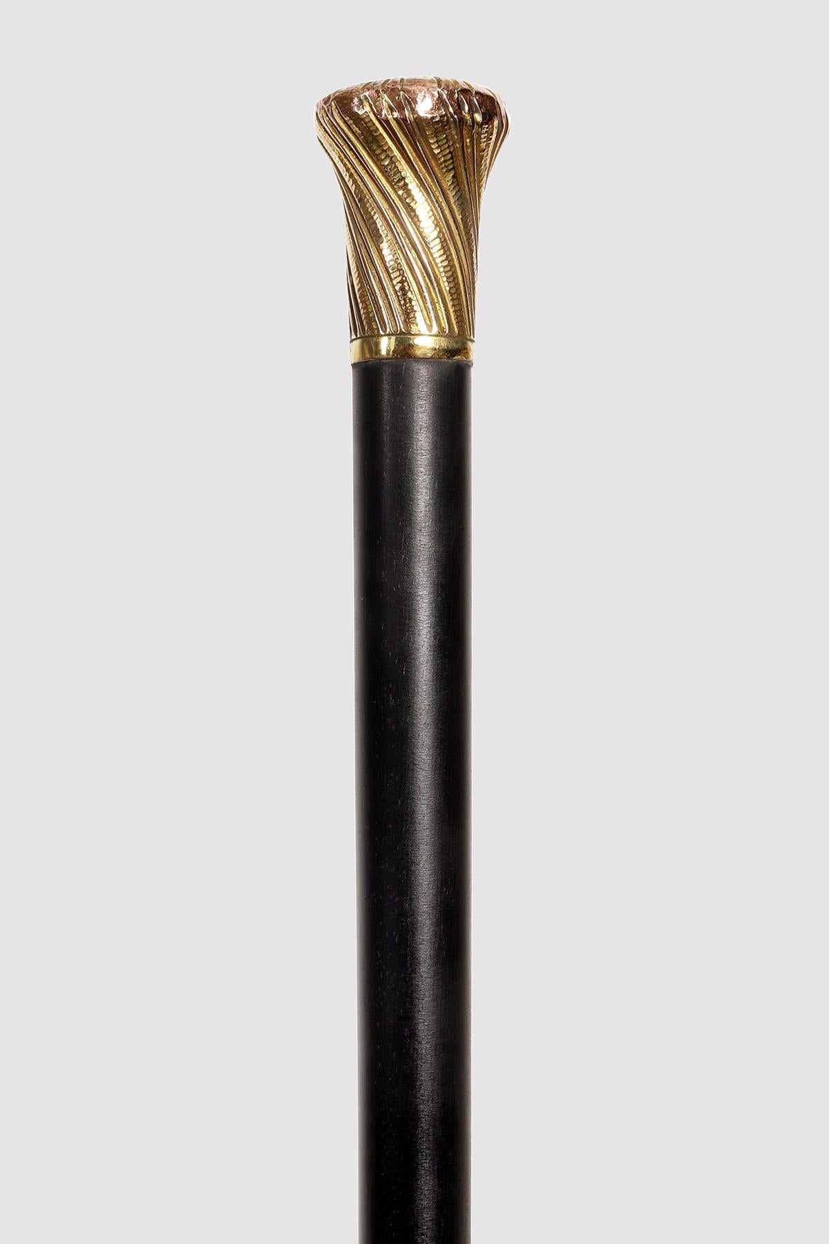 Walking stick with tip in white metal and iron. The shaft is ebony and the diameter gradually widens up to the pommel. The shape is that of the milord pommel, in gilded copper, with embossed decoration of twisted lines that meet in the center of the