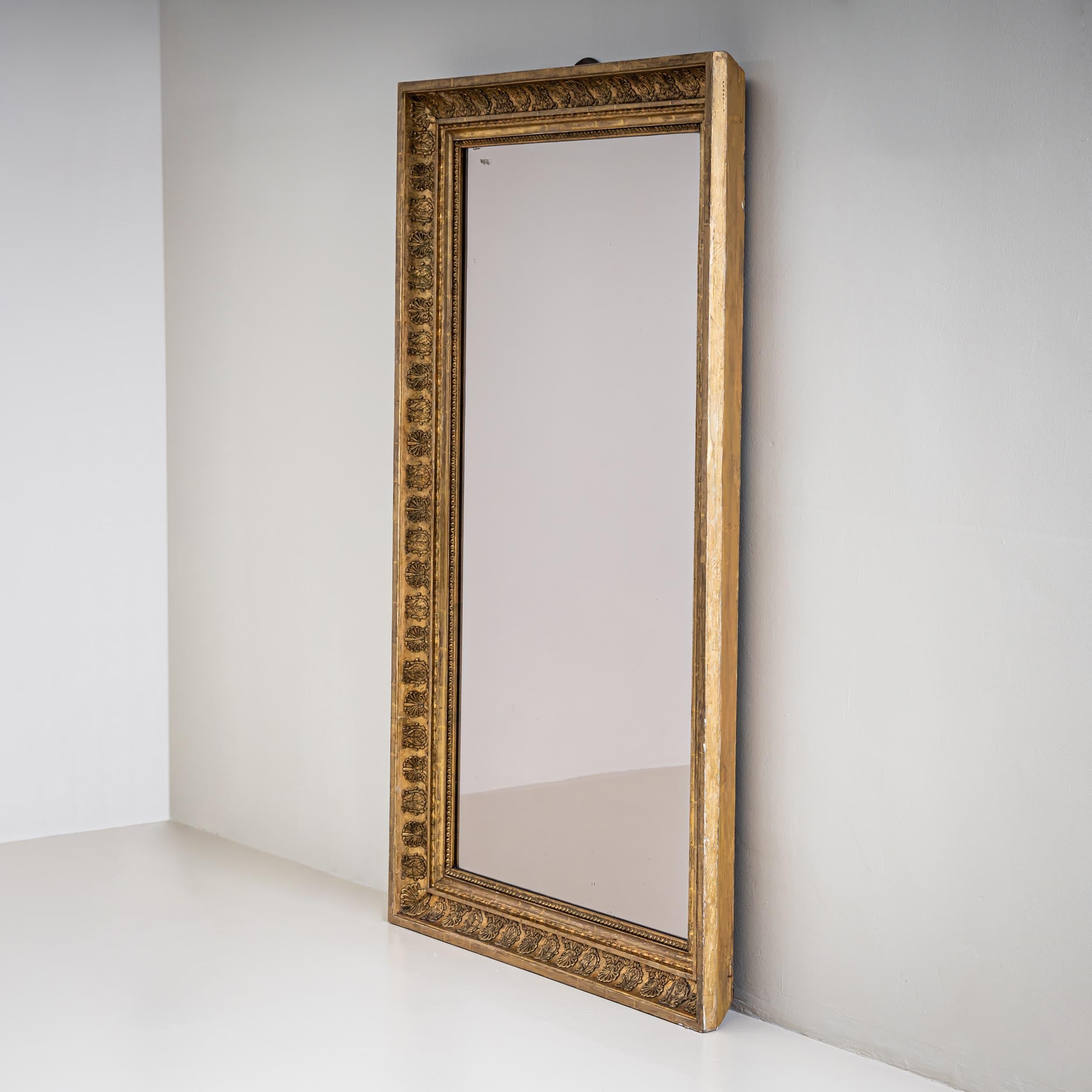 Miroir mural profilé de style Empire avec un cadre rectangulaire et des décorations appliquées de feuilles d'acanthe. La surface est entièrement dorée et présente une patine élégante. Le verre du rétroviseur a été remplacé.