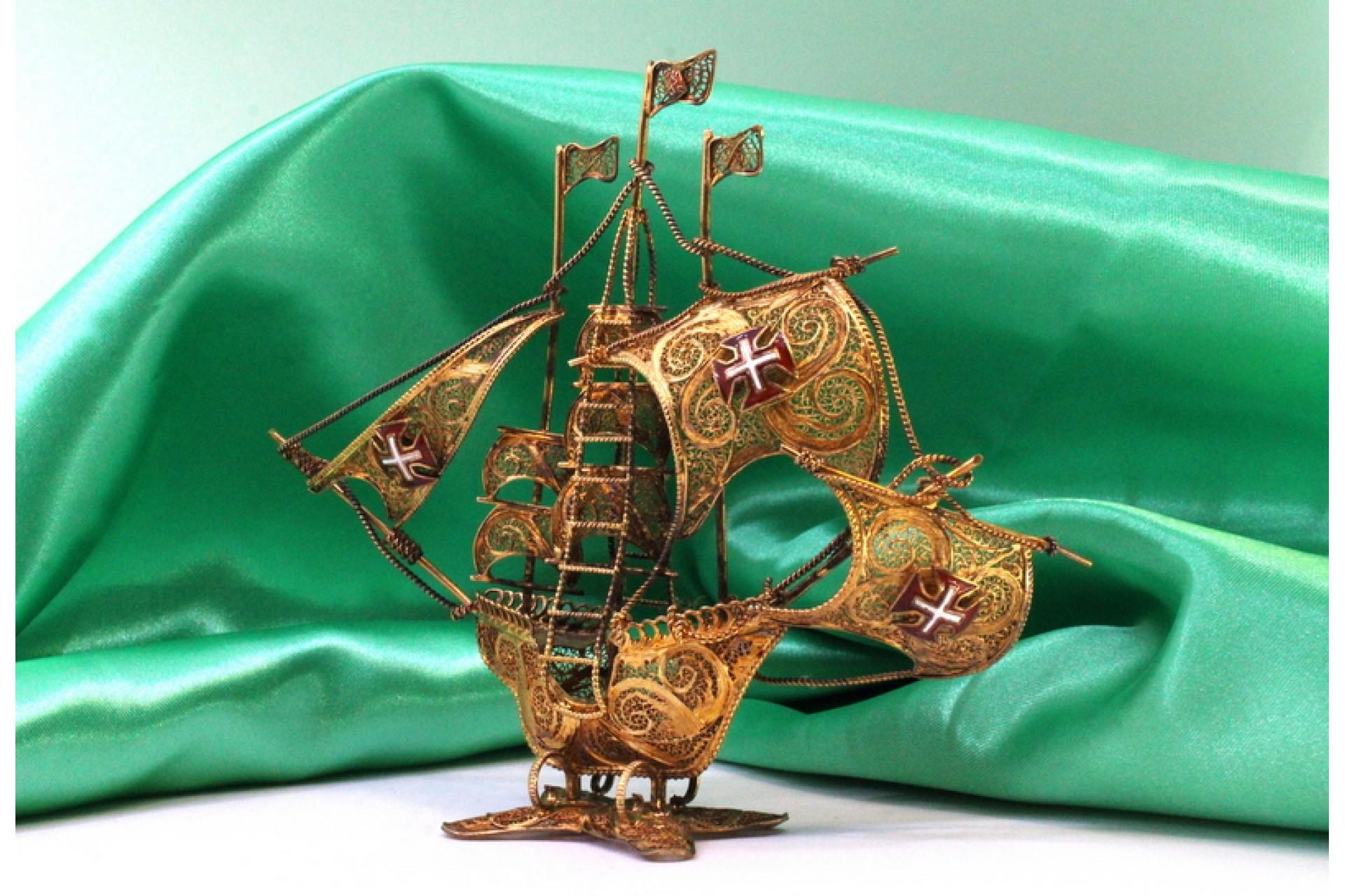 Description: Silver caravel with gilded filigree, with the Portuguese coat of arms on the sails and resting on a cut-out base. Metal: Silver. Origin: Portuguese. Mark: Eagle's head. Weight: 61.99 grams. Dimensions: 14.5cmx12cm. Content: 833/1000.