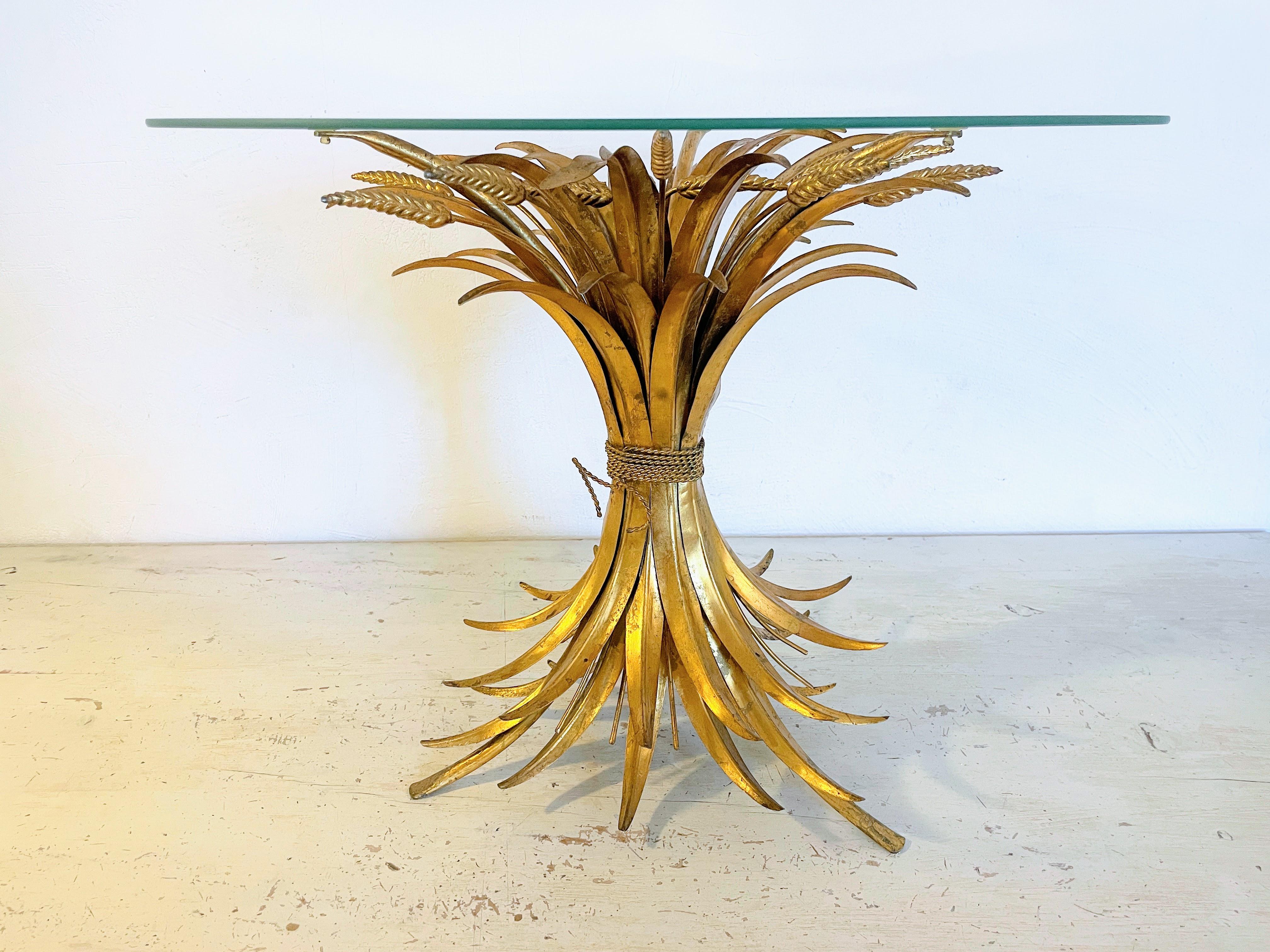 ntroducing a captivating Hollywood Regency 'Ears of Wheat' Coffee Table, originating from the glamorous era of the 1950s. This exquisite table boasts a gold-colored, intricately adorned base, skillfully crafted in the form of a sheaf of wheat, an