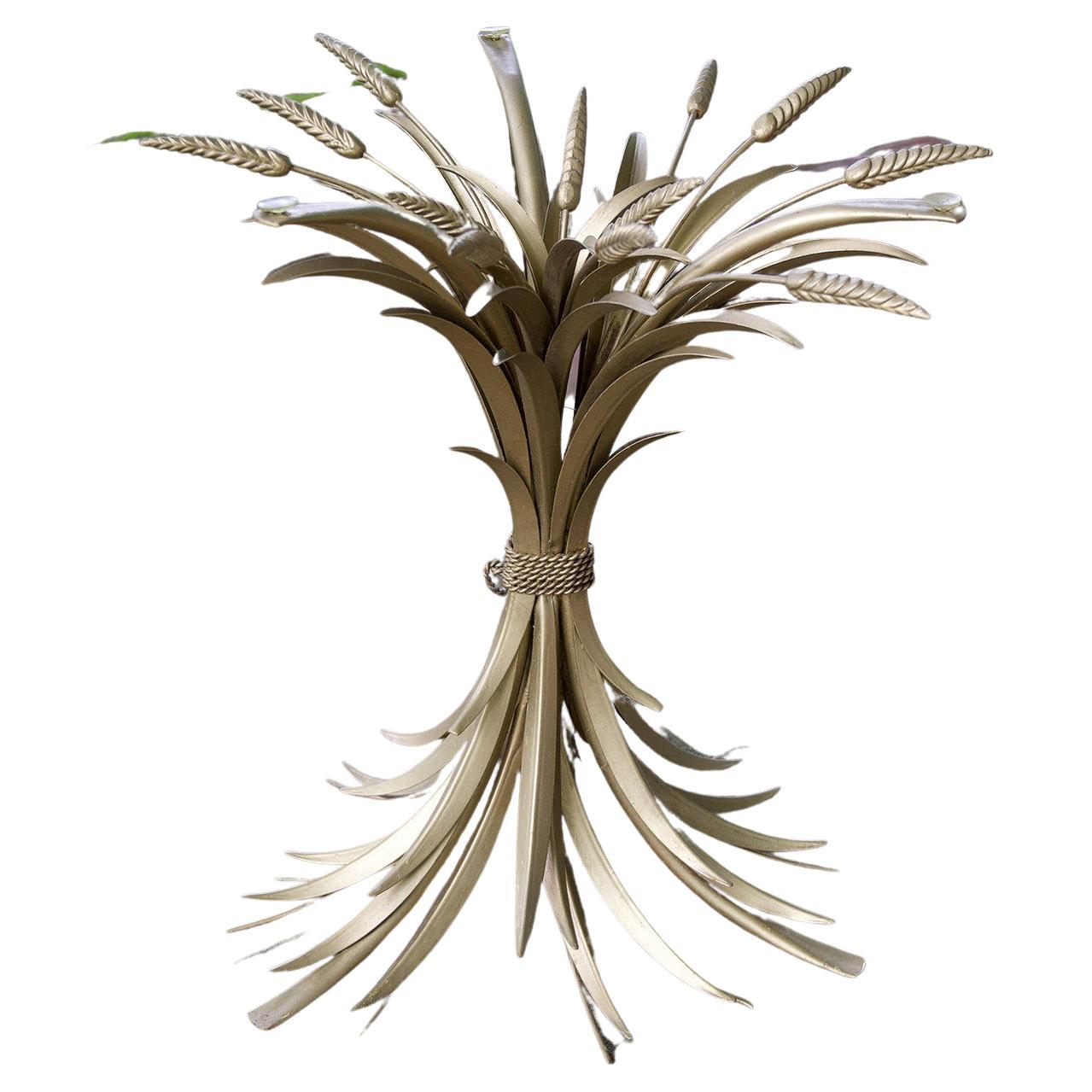 An occasional table in the Hollywood Regency style, the gilded brass base in the form of a stylized sheaf of wheat tied with a cord, the sheaf flared at top and bottom and supporting a circular glass top, American, ca. 1960. Measures: 22 ins. high,