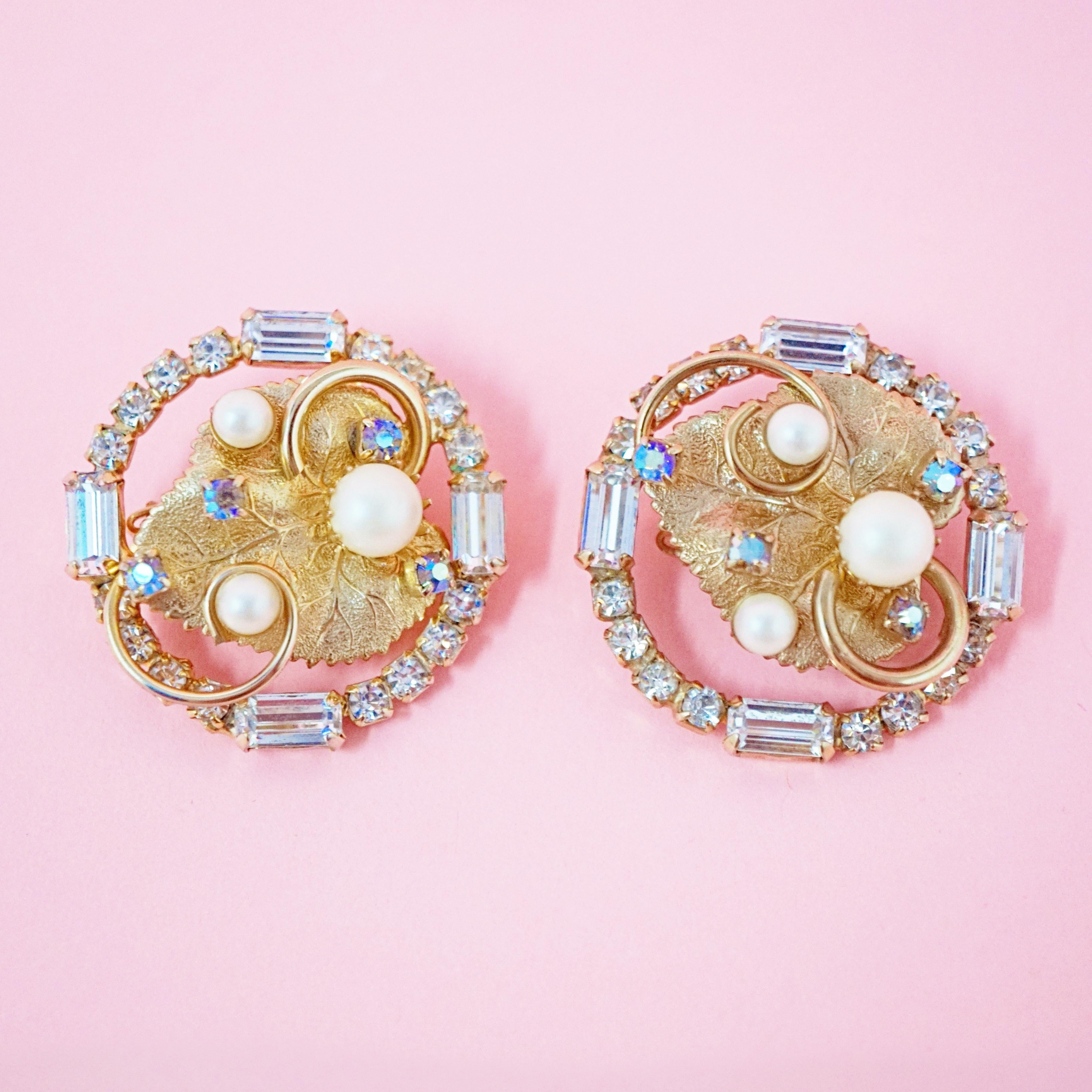 These gorgeous Hobé clip-on statement earrings, circa 1950s, are one of the brand's more fun and unique designs.  A gold-plated leaf is decorated with gilded swirls, faux pearls and Aurora Borealis crystals.  This centerpiece is surrounded by a halo