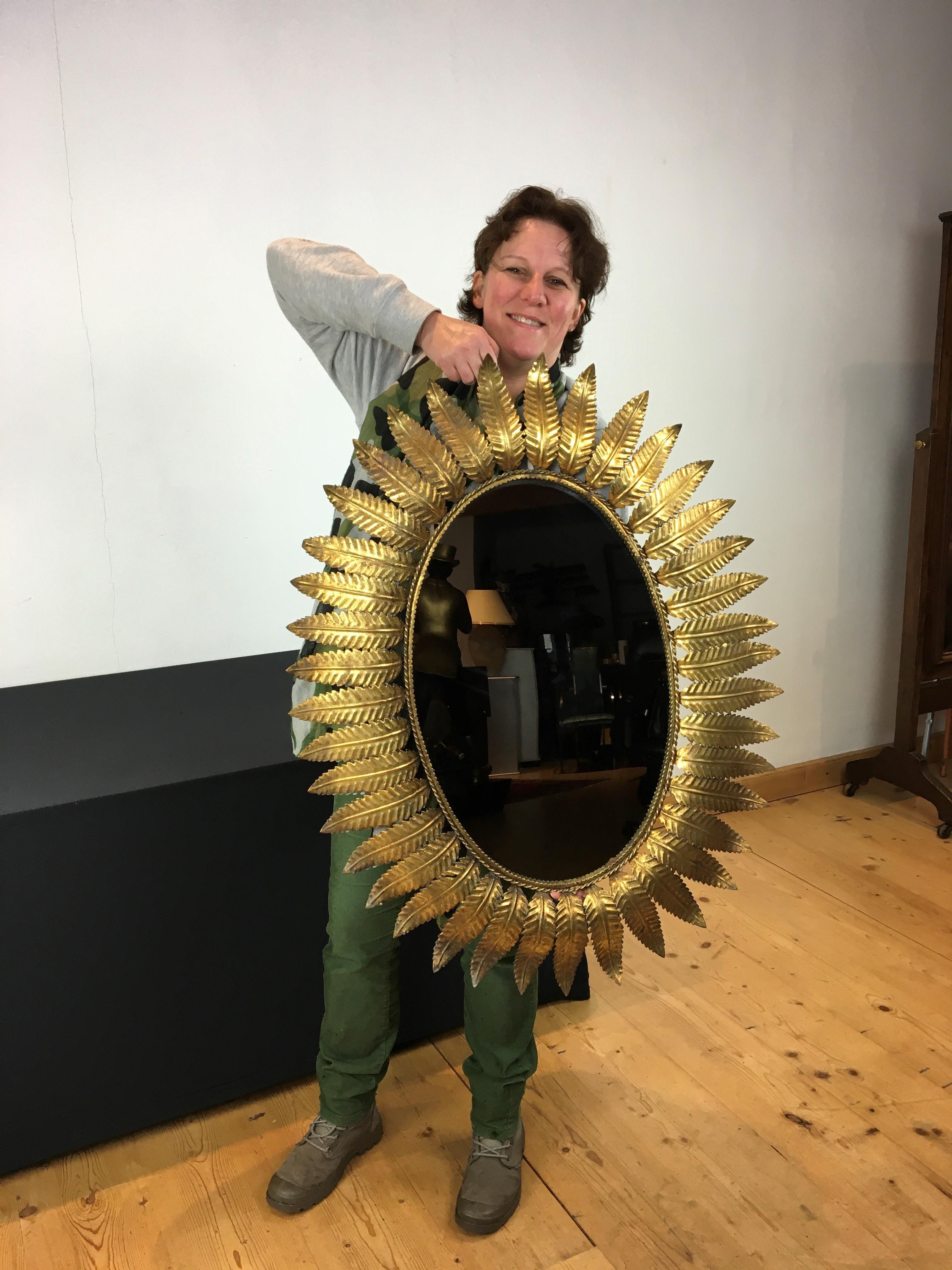 Great looking gilded metal oval mirror with leaves all around. 
A stylish oval wall mirror - sunburst mirror with gold leaf finish which is dating from the period 1950 - 1960. A Spanish mirror with gilt leaves with a great patina by age and use.