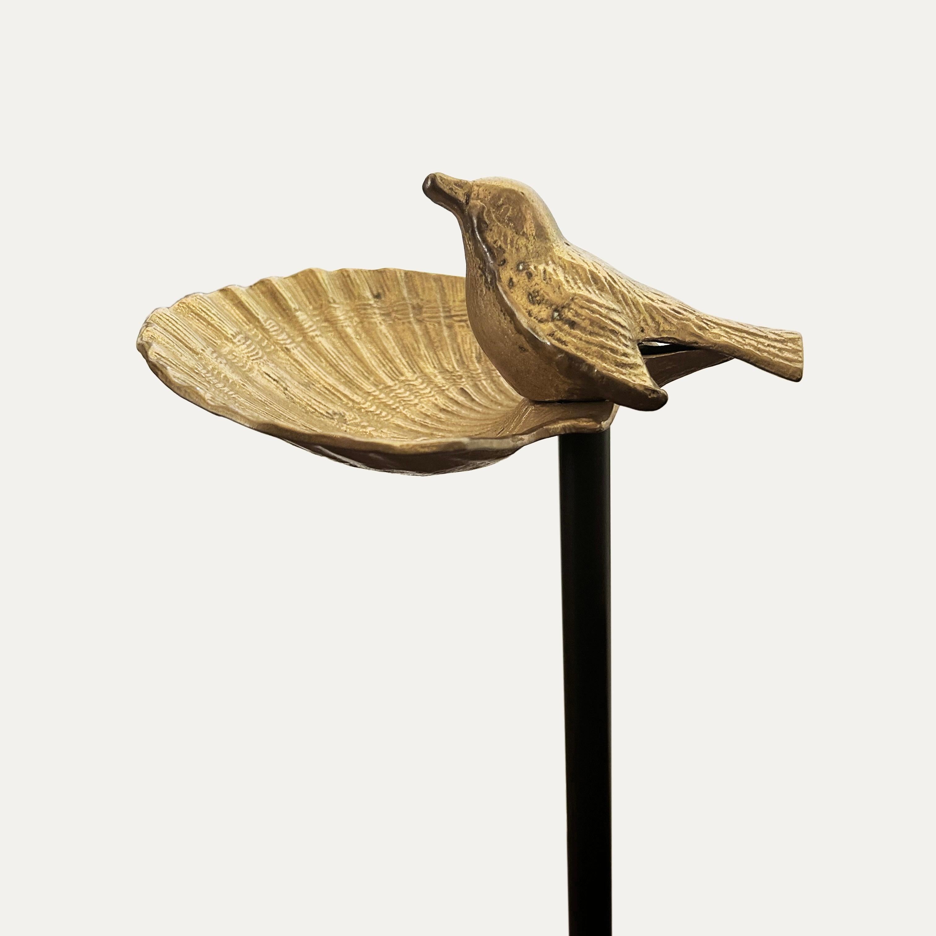Videopoche in metallo dorato raffigurante una conchiglia con un uccello appollaiato, su una base decorativa a treppiede di ramoscelli e foglie. 