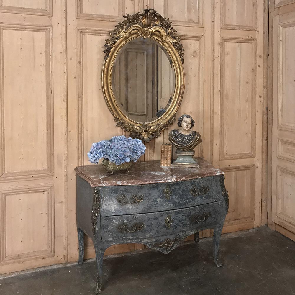 19th century French Louis XVI gilded oval mirror is poised to create a lavish decorative touch to any room, with its elaborate stylized shell, floral and foliate motifs above and below, and subtly embossed frame in between, all surrounding the