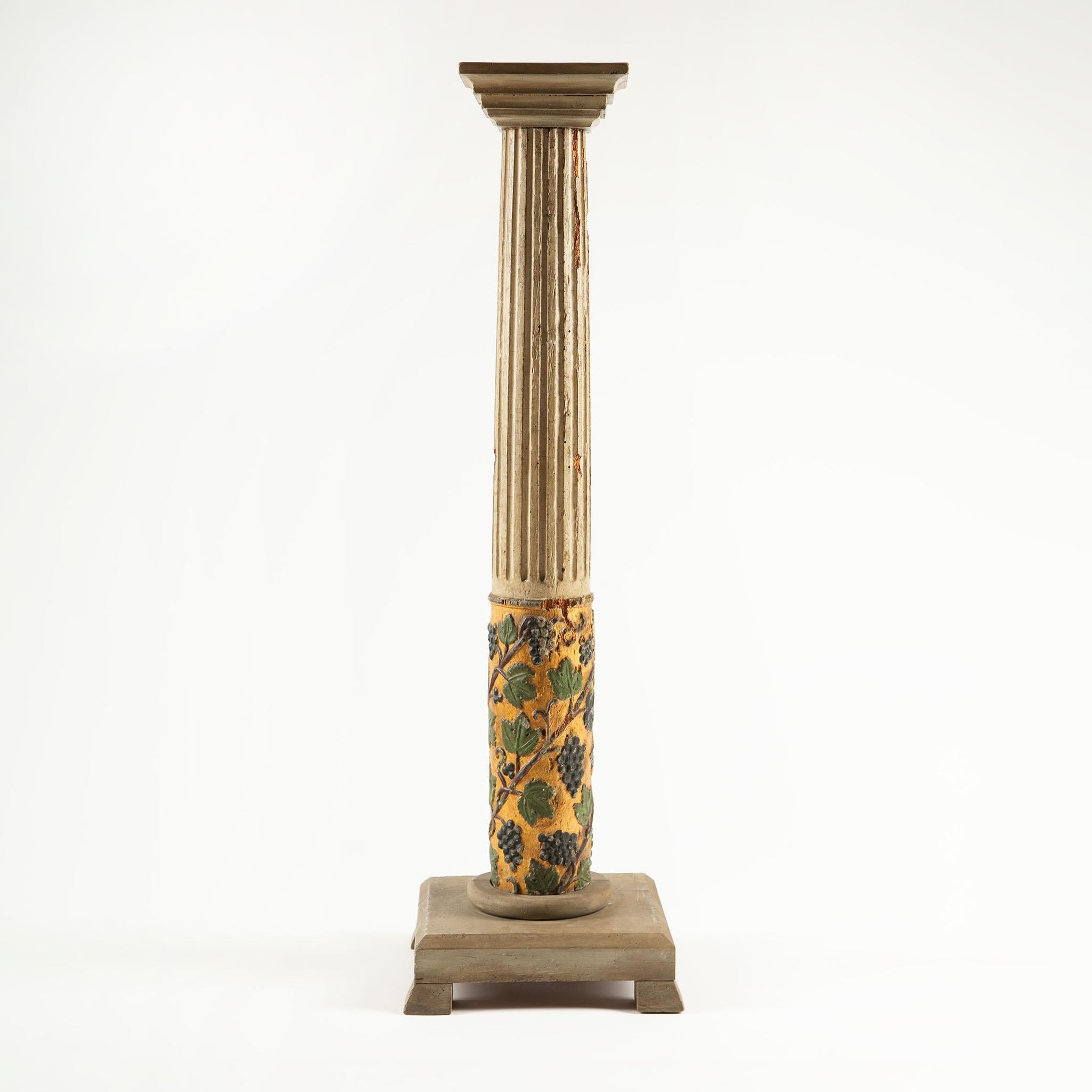 Column-shaped sellette in painted and gilded wood, featuring a fluted shaft topped with a square molded abacus and accented at the lower section with richly carved and polychrome grapevines, leaves, and clusters of grapes against a golden ground.