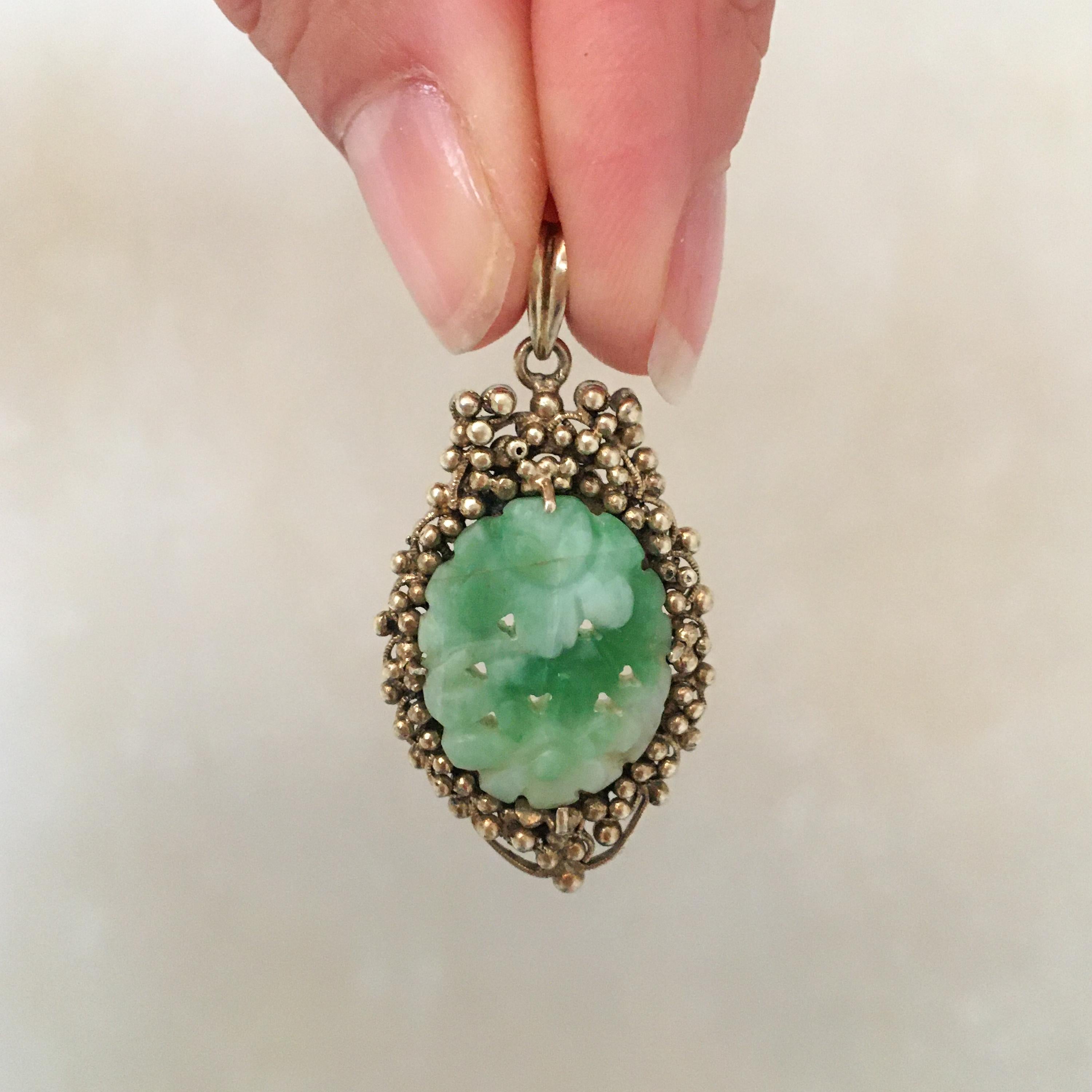 A gilded silver floral and fruit carved jade pendant. The mottled white and green jade is carved into a floral design. The green and white floral carved jade is set between prongs surrounded by the grapes which are made of gilt silver. The exterior