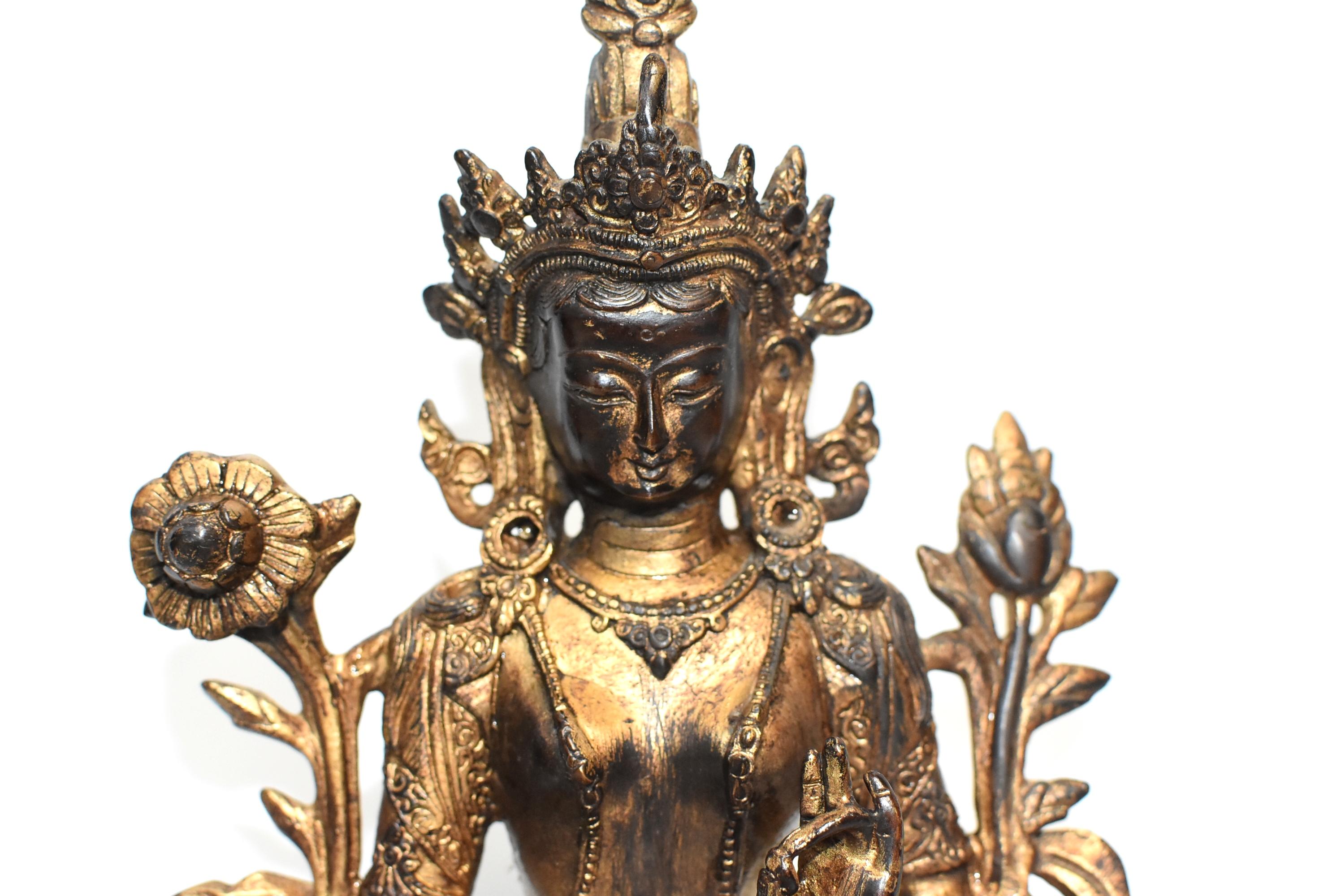 A beautiful, large, gilded Tibetan Tara statue. The Green Tara is seated on a lotus throne, wears a highly decorated crown and is decorated with sashes and flowers. Her body is draped with lariats of pearls, her right foot extends over the boundary