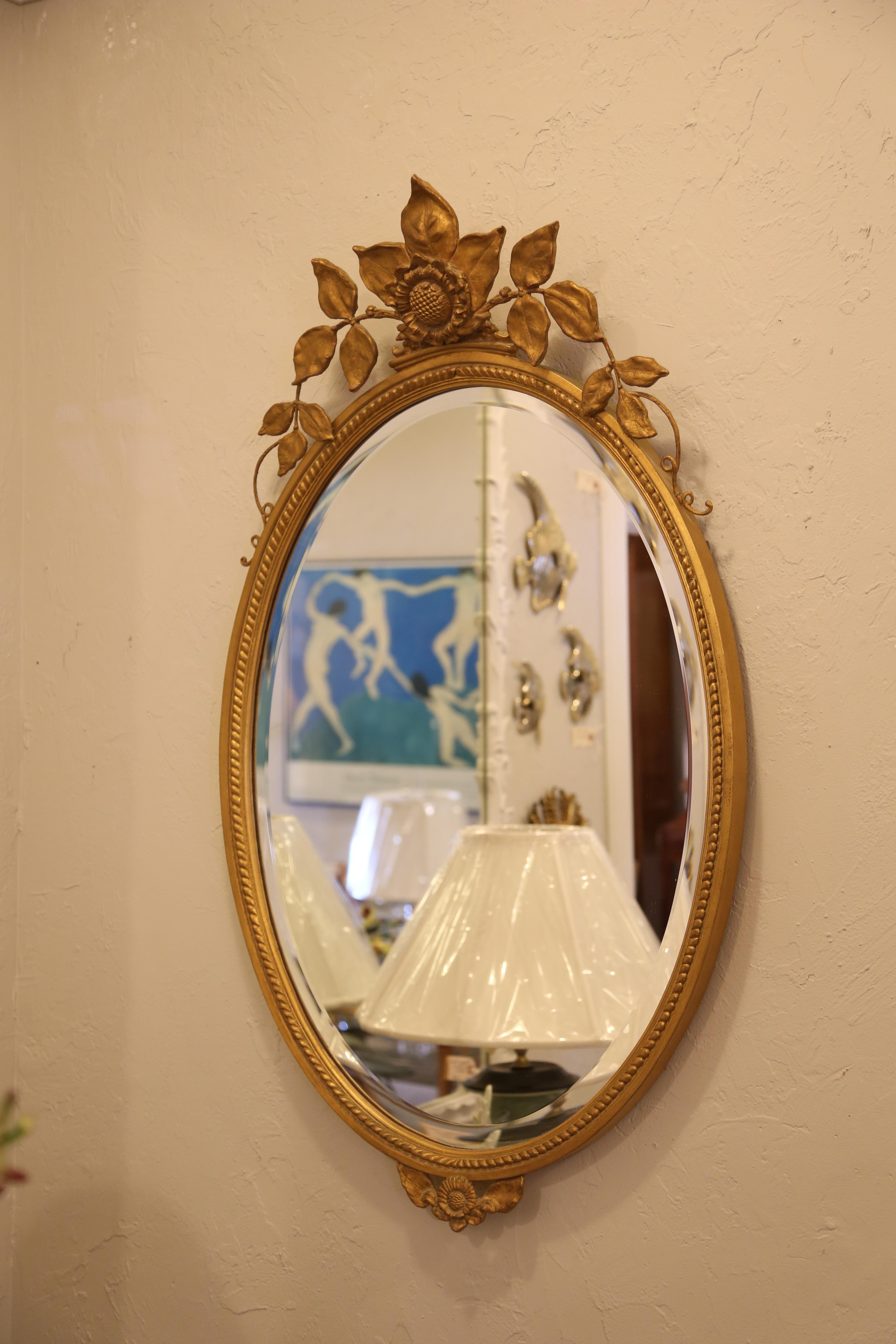 Oval gilded mirror adorned with petals and topped with a sunflower. Created by Carol Canner for Carvers Guild.