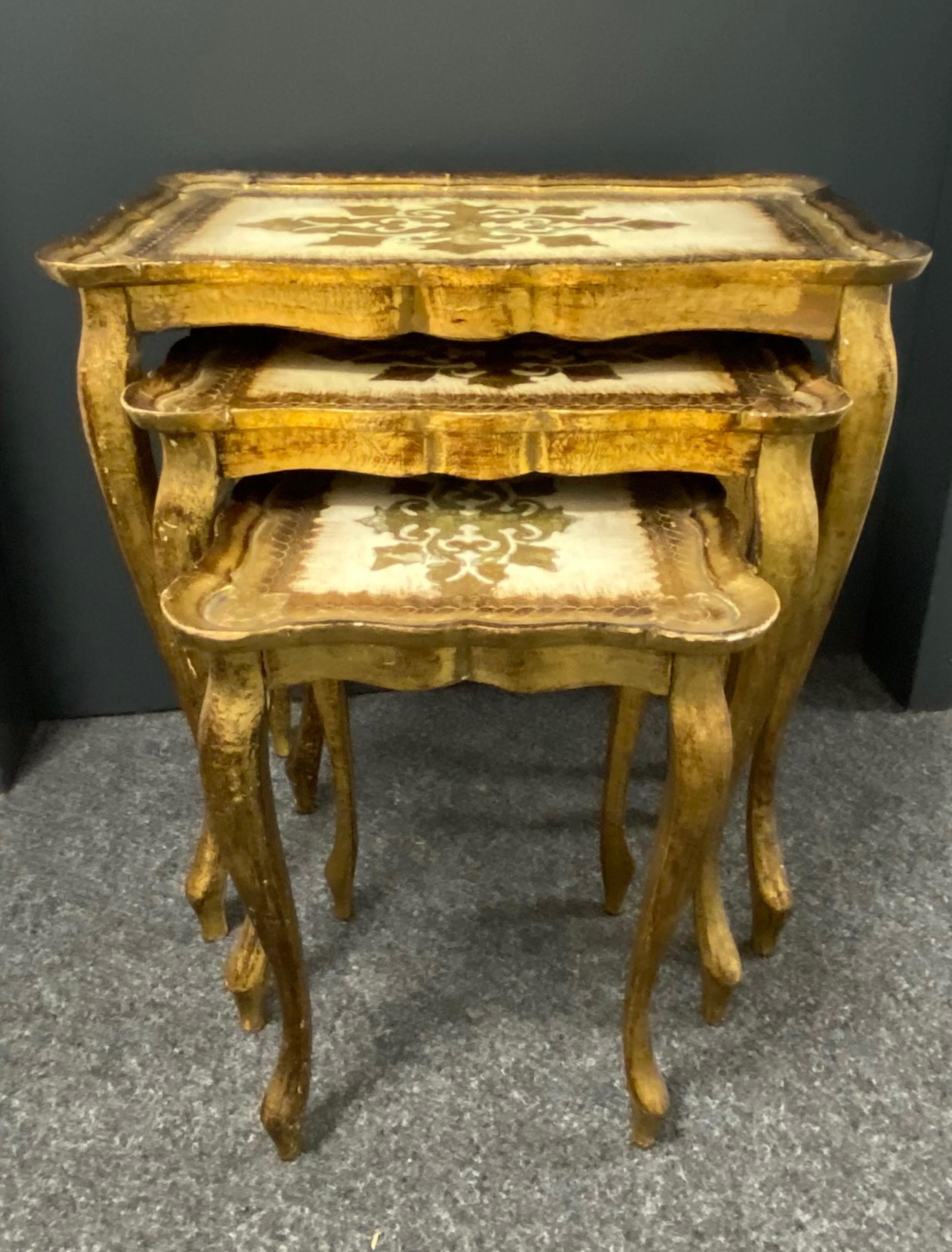 This set of three Florentine-style nesting tables was made in Italy, circa 1960. They feature cabriole legs and intricate hand painted details on the tabletops with scalloped edges. The gilded wood has a beautifully weathered patina. These pieces