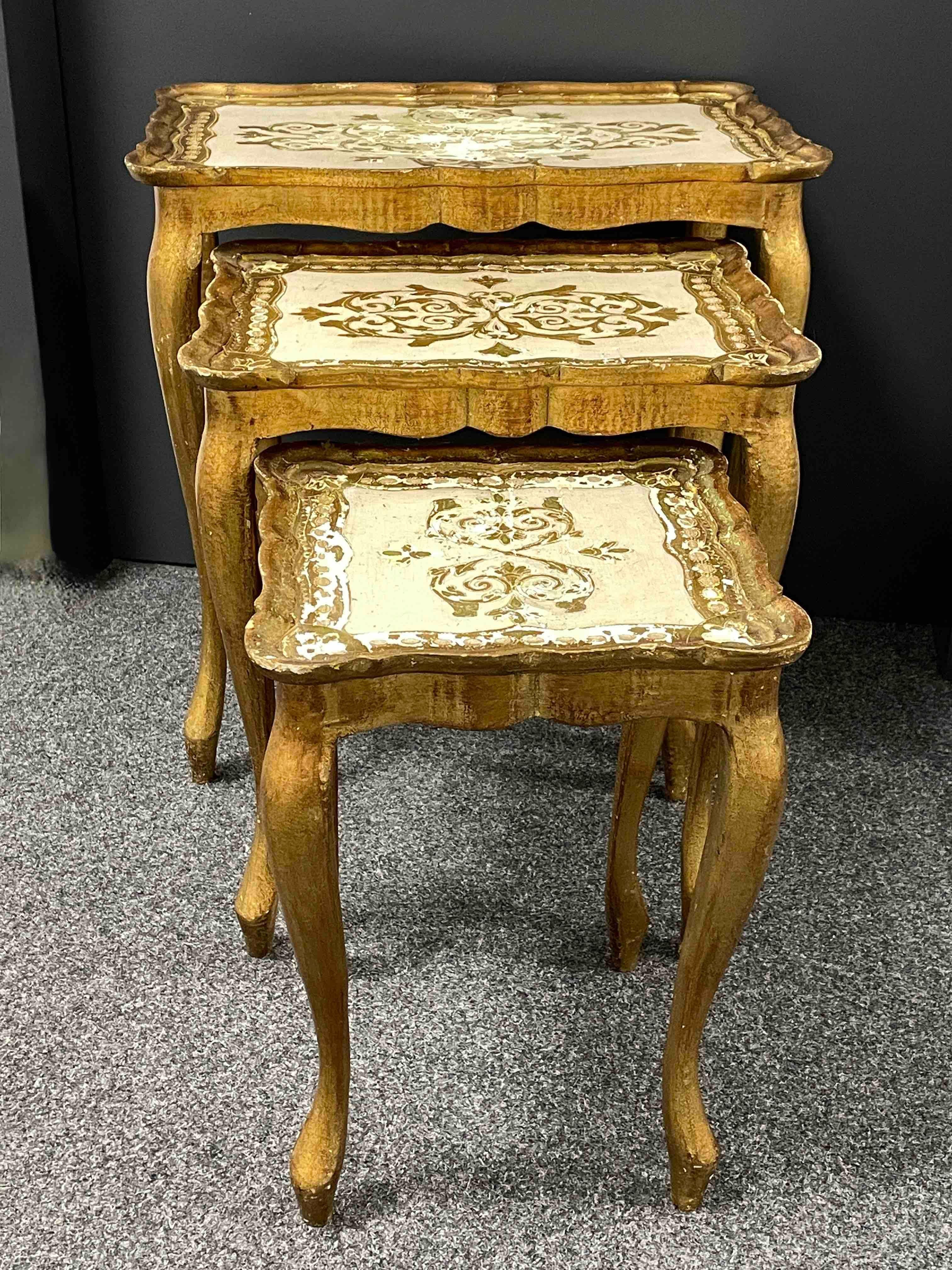 This set of three Florentine-style nesting tables was made in Italy, circa 1960. They feature cabriole legs and intricate hand painted details on the tabletops with scalloped edges. The gilded wood has a beautifully weathered patina. These pieces