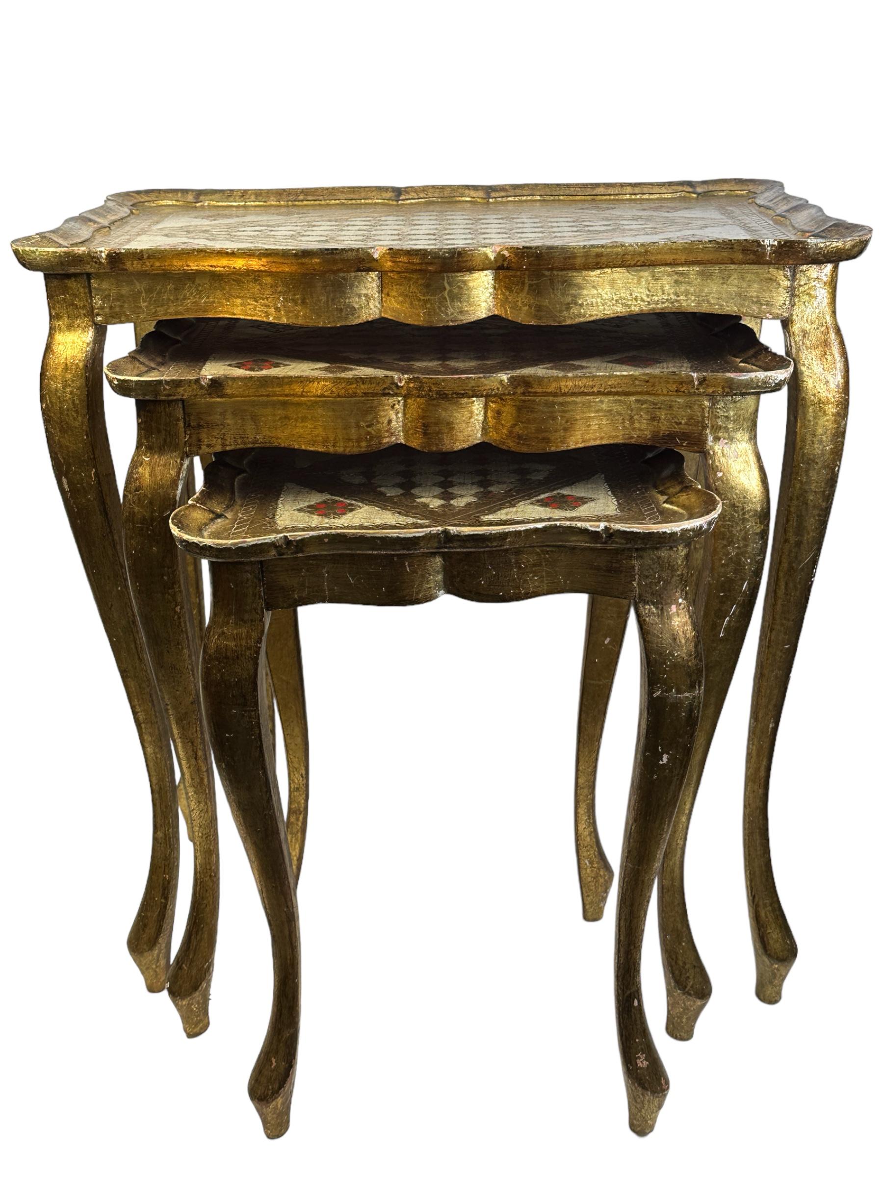 This set of three Florentine-style nesting tables was made in Italy, circa 1960. They feature cabriole legs and intricate hand painted details on the tabletops with scalloped edges. The gilded wood has a beautifully weathered patina. These pieces