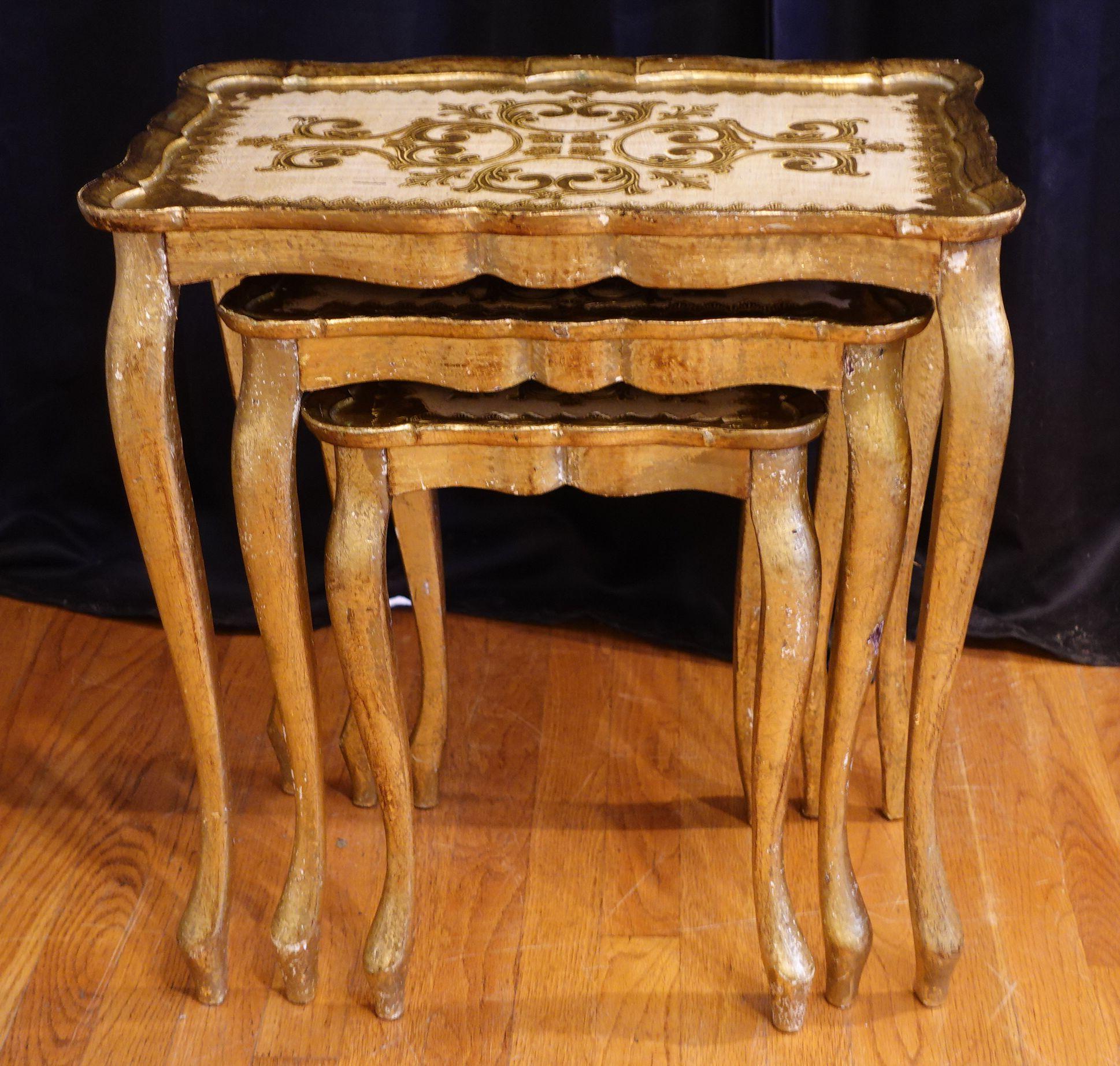 Three Florentine-style nesting tables were made in Italy, circa 1960. They feature cabriole legs and intricate hand-painted details on the tabletops with scalloped edges. The gilded wood has a beautifully weathered patina. The tall table is approx.