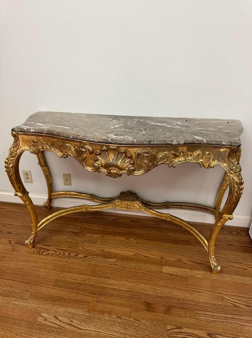 A beautifully executed Louis XV-style console table featuring an ornate giltwood frame and a substantial marble top. This late 20th-century interpretation captures the elegance of classic French Rococo design, from its serpentine apron to its finely