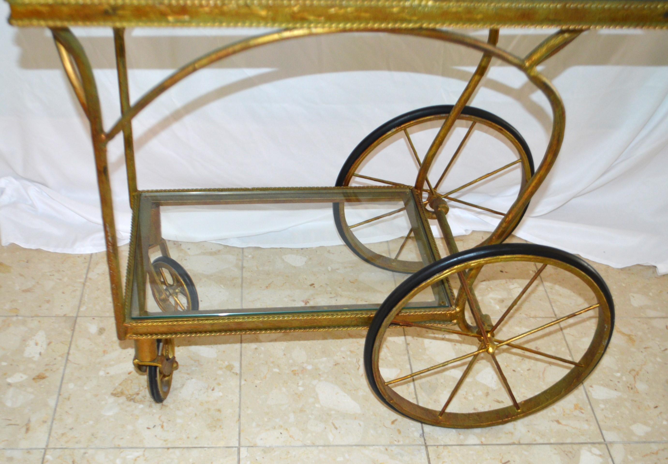A Belle Époque Wrought  Iron Bar Cart having two levels, both with glass tops in good condition. To note is the decorative design of the molding around the glass.. There are two sets of wheels, the large one are working very smoothly, the smaller