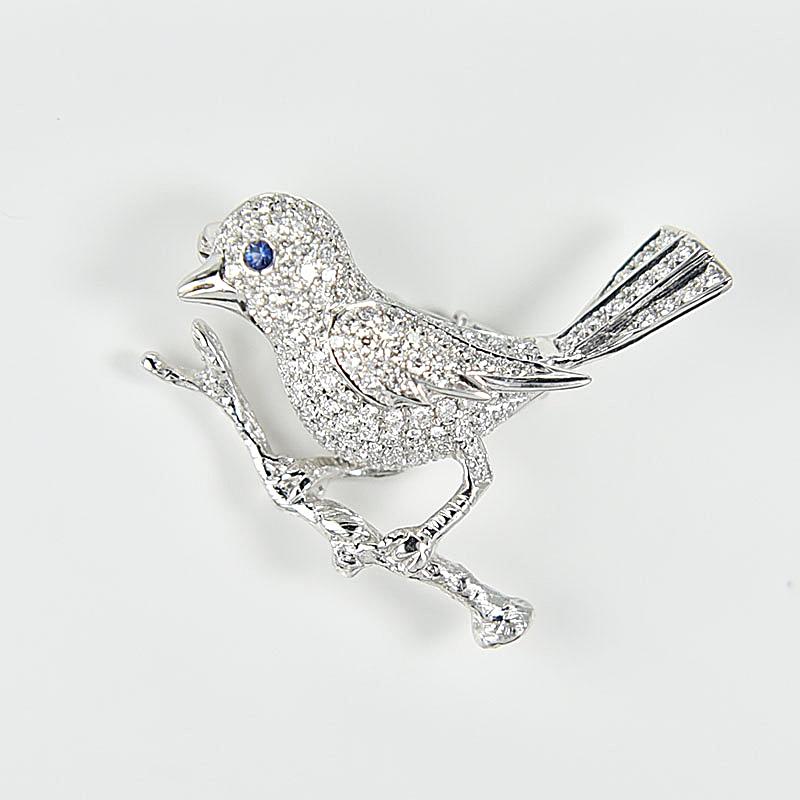 A delicate 18 Karat diamond brooch of bird design, with the tree branch handcrafted to create a sense of reality. This nature motif is given to life with a drop of sapphire blue.
There are a total of 144 diamonds weighing approximately 0.93 carat,