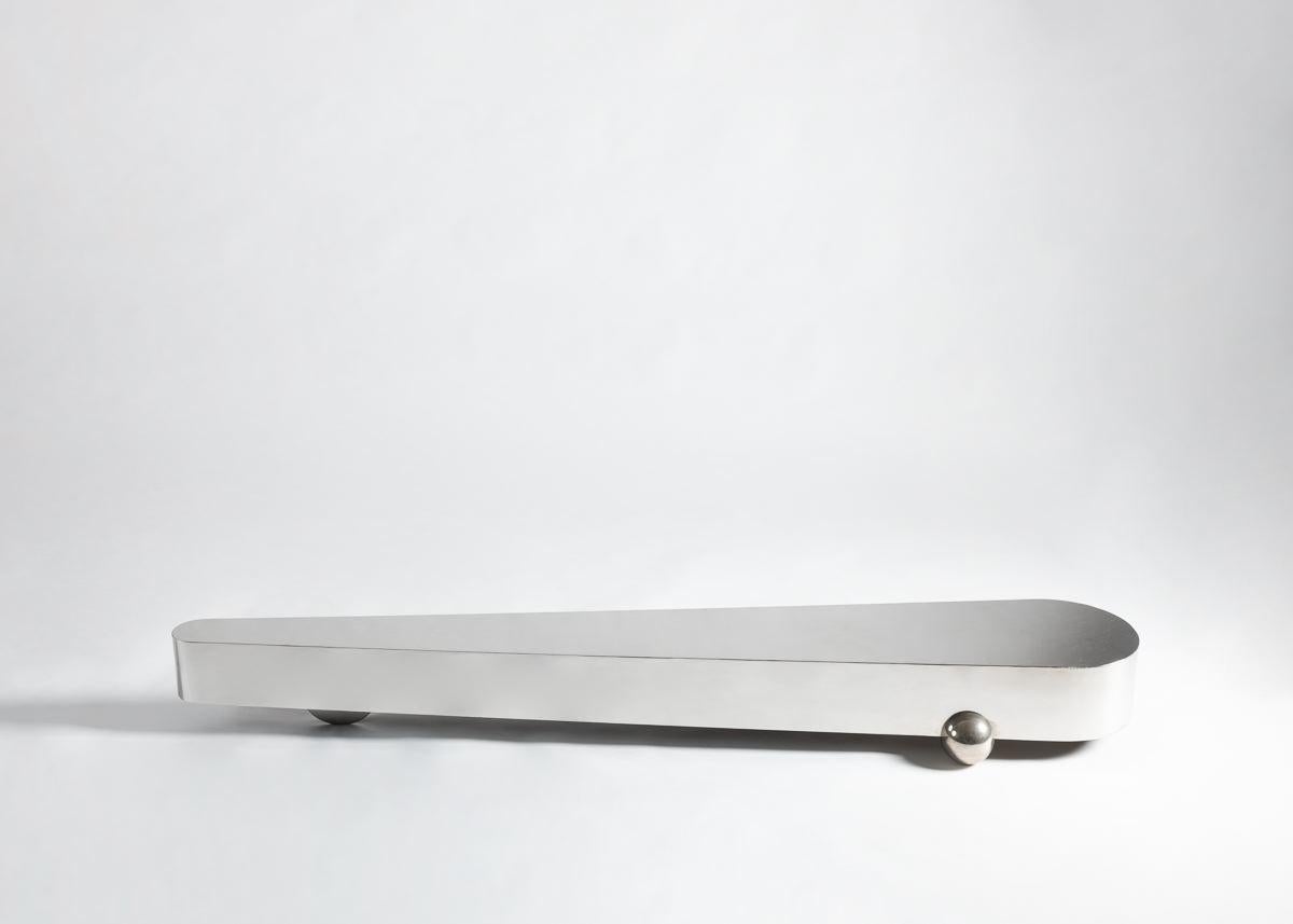 This sleek, stainless steel piece by Gilles Derain rests on two spherical shaped feet and a hidden support where one end narrows to a rounded point. It is veritably unique, breaking from all established expectations of what a coffee table is