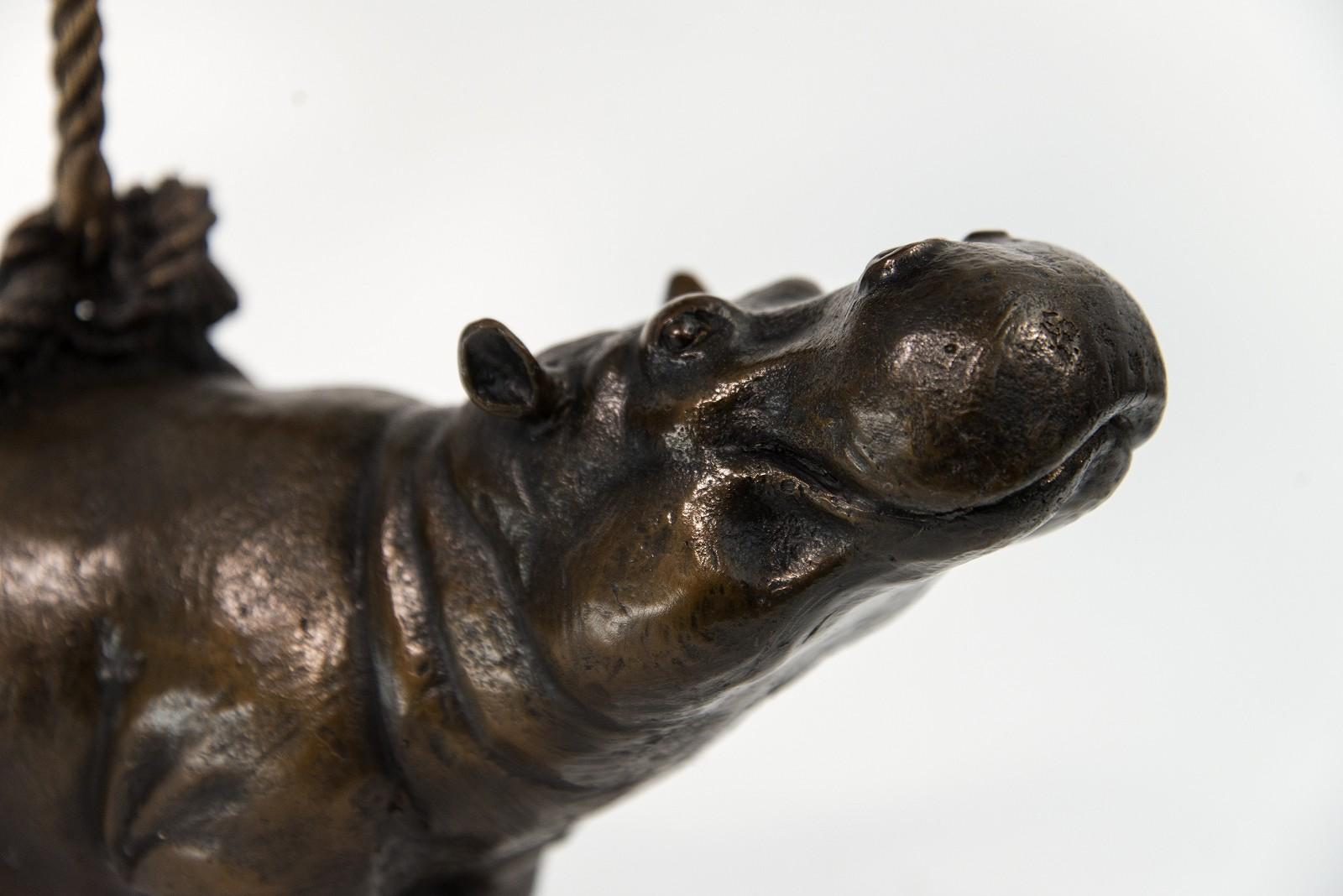 In classic bronze, two hippos facing opposite directions, one suspended over the other are joined by a rope in this fun table-top sculpture by Australia’s artistic duo, Gillie and Marc. Hippos are one of several vulnerable species that the couple