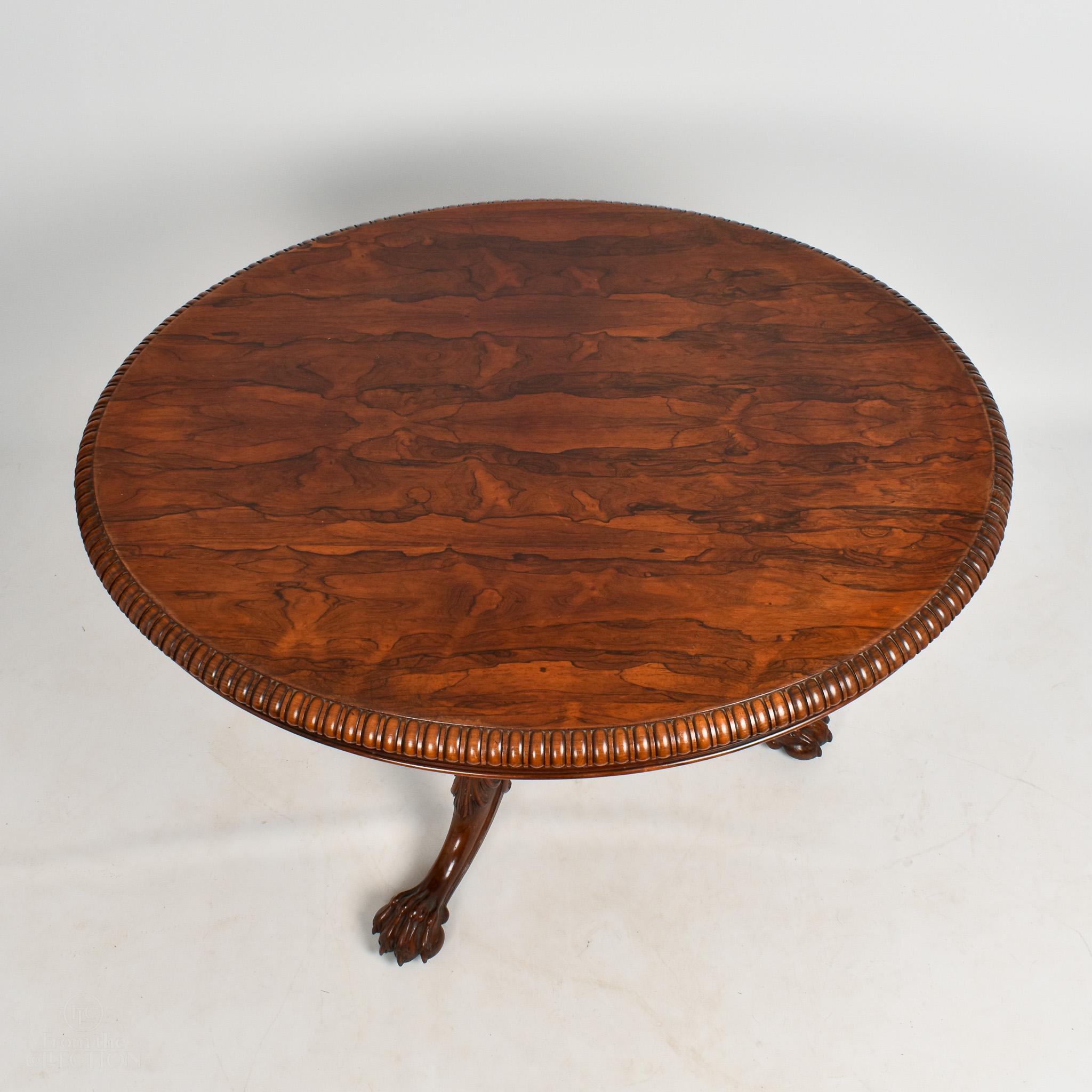 This stunning rosewood oval centre table (circa 1840) is made from a beautiful dark wood and is in excellent condition. Stamped Gillows and with beautiful carved gadrooned edging. Centre pedestal down to three splayed legs with claw feet on brass