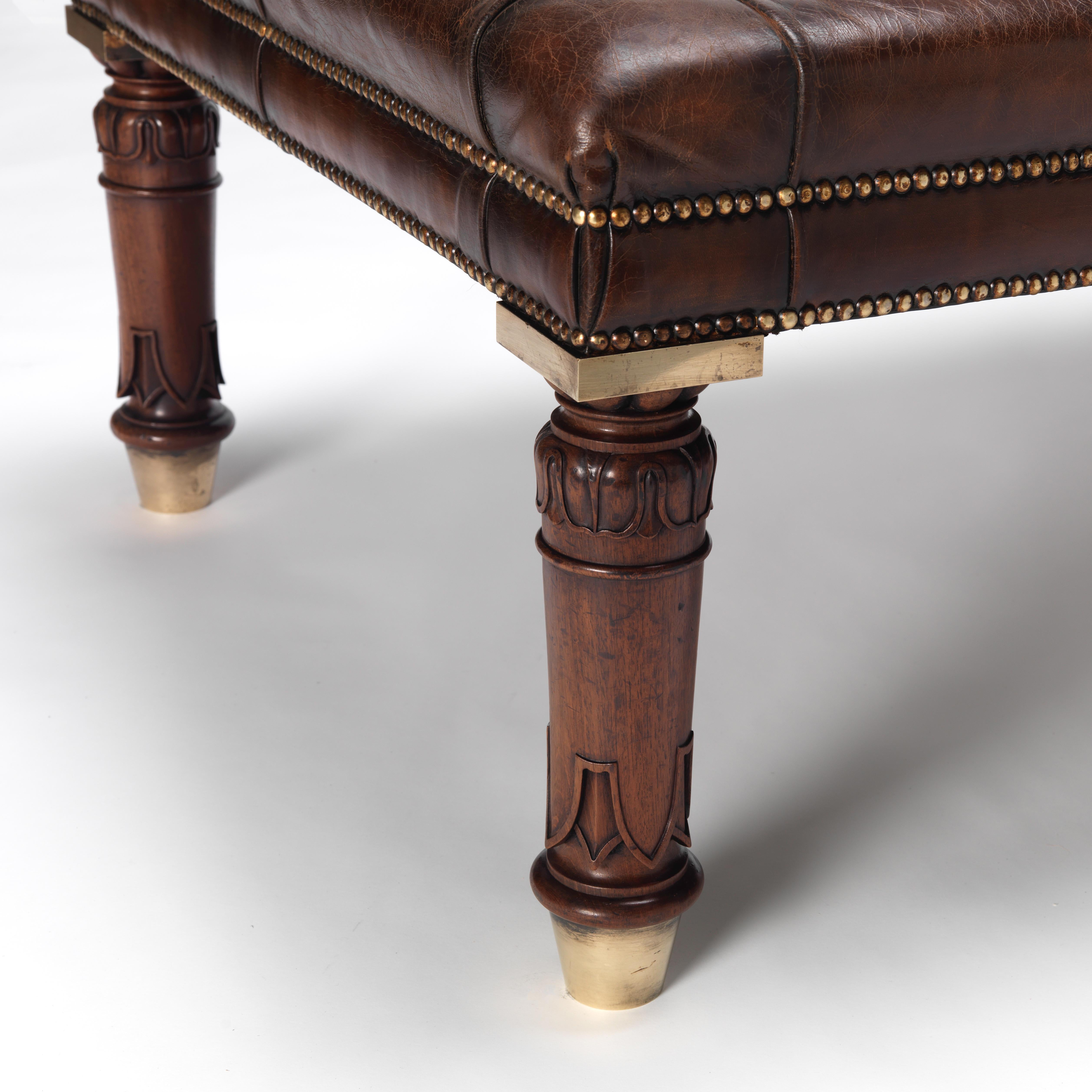 A finely carved mahogany Gillows design library stool/ coffee table. Turned and stylised acanthus leaf decorated legs with a solid brass top block to leg and tapered brass shoe. Shown upholstered in hand aged leather with military buttons and aged