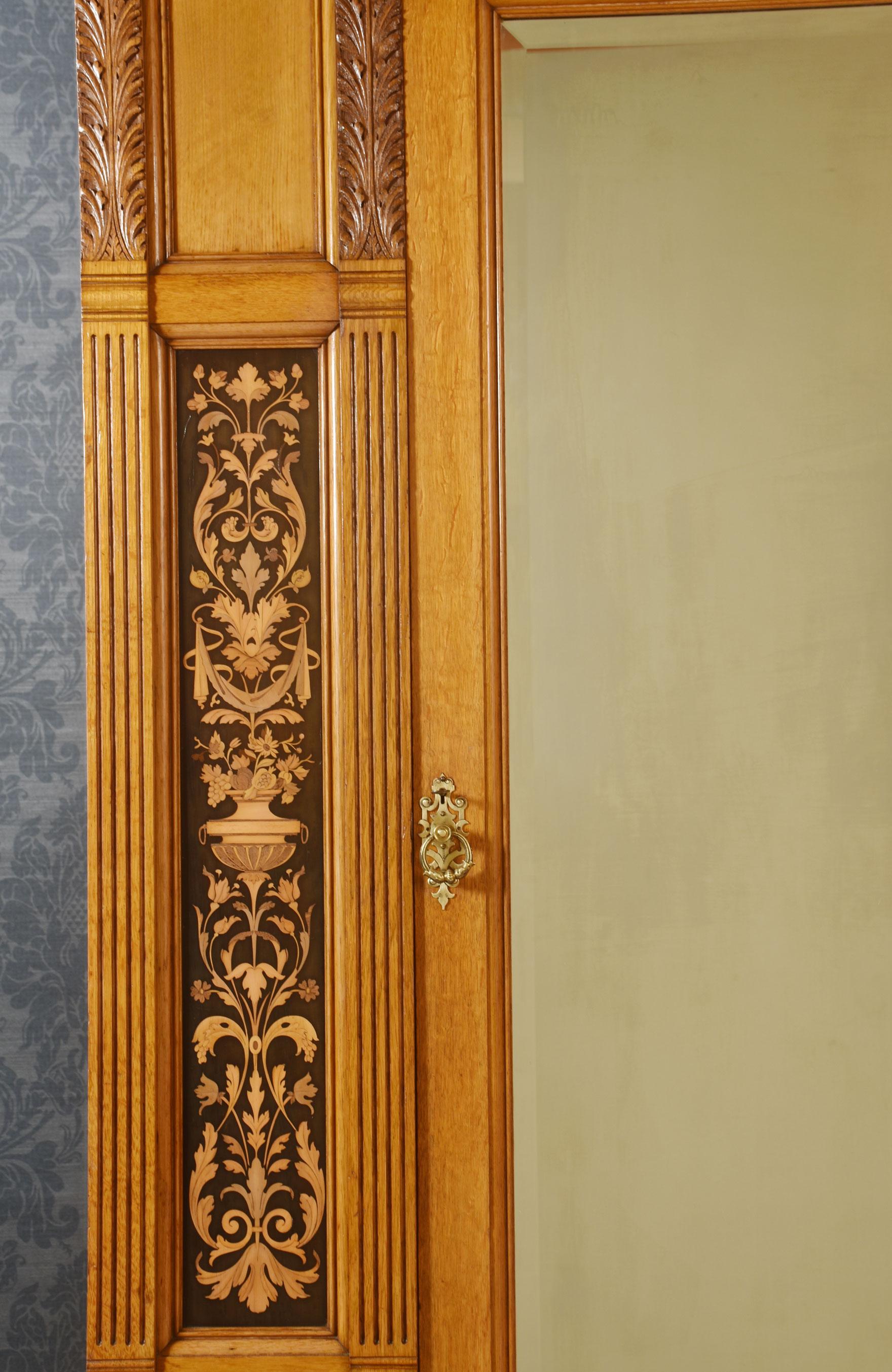 Gillows of Lancaster marquetry inlaid oak wardrobe, having carved moulded cornice above large original bevelled mirror door opening to reveal an upholstered interior with large hanging rail. Flanked by ebonised panels with scrolling floral marquetry
