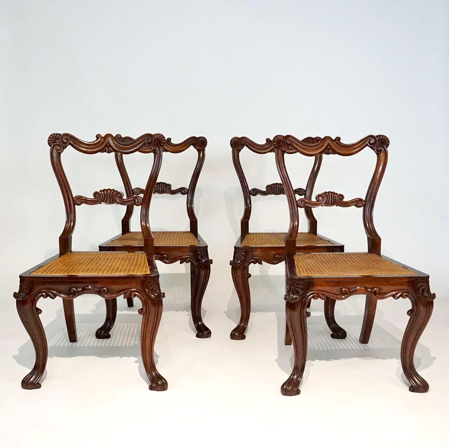 An exquisite set of four English George IV circa 1825 'First' Rococo Revival style side or dining chairs all signed by the legendary cabinetmaking firm Gillows of Lancaster having foliate and anthemion carved rosewood frames with caned seats.