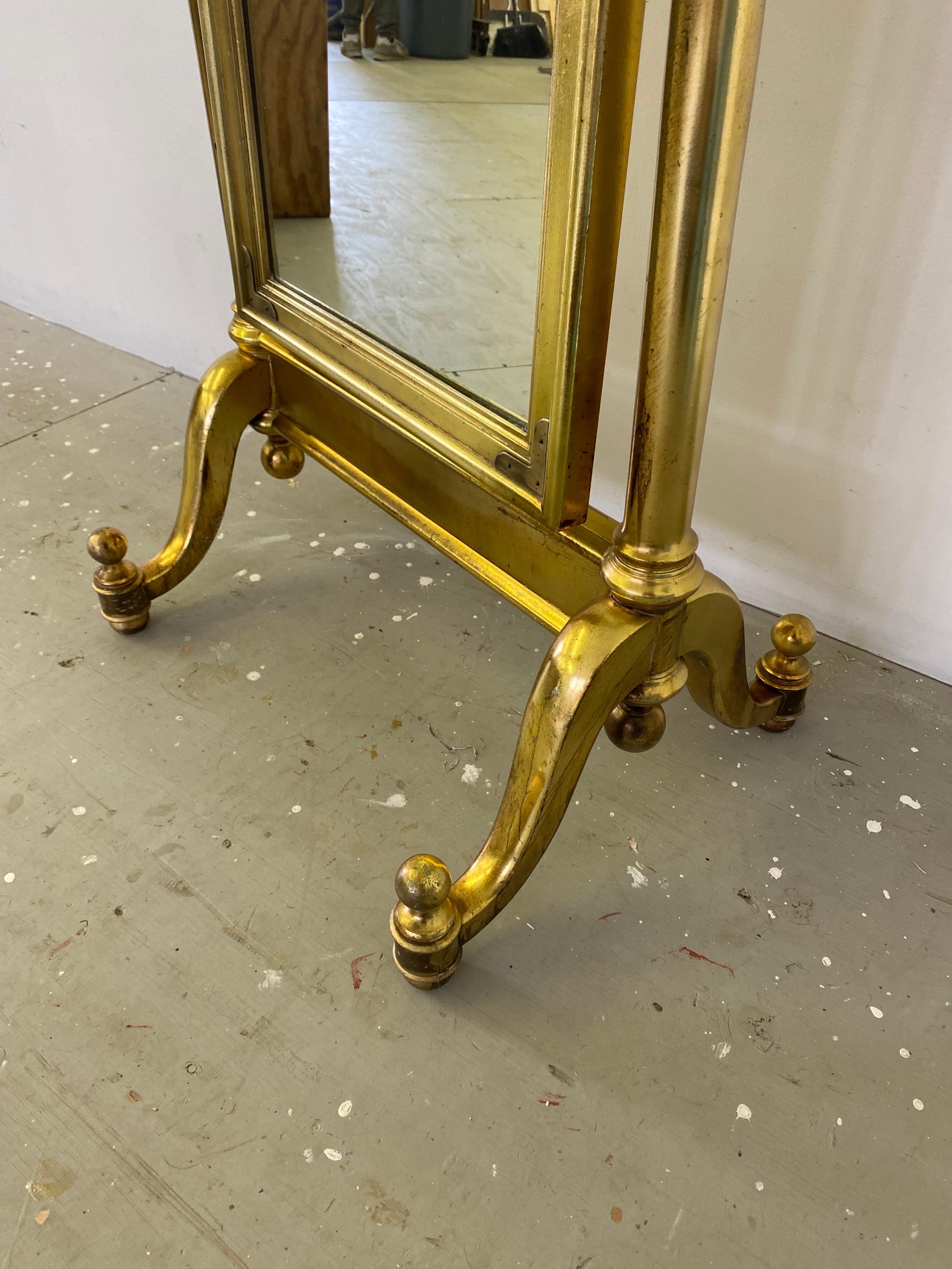 Gilt Cheval Mirror. Dates to the 1970's with Brass Campaign Style Brackets in the Corners. Has the look of Brass with a Twist! Little Gilt loss and some staining. Overall a very nice amount of Patina! Stands very Solid!.
