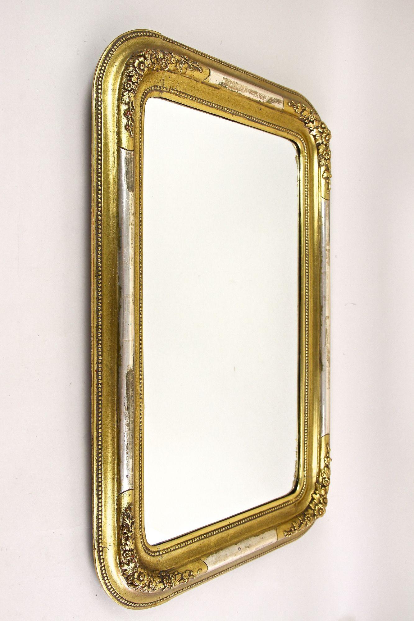 Charmant miroir mural Biedermeier doré du 19ème siècle d'époque en Autriche vers 1840. Se distinguant par ses jolis stucs floraux, ses demi-barres argentées (légèrement abrasées) et ses coins arrondis, ce cadre a été restauré par nos experts en